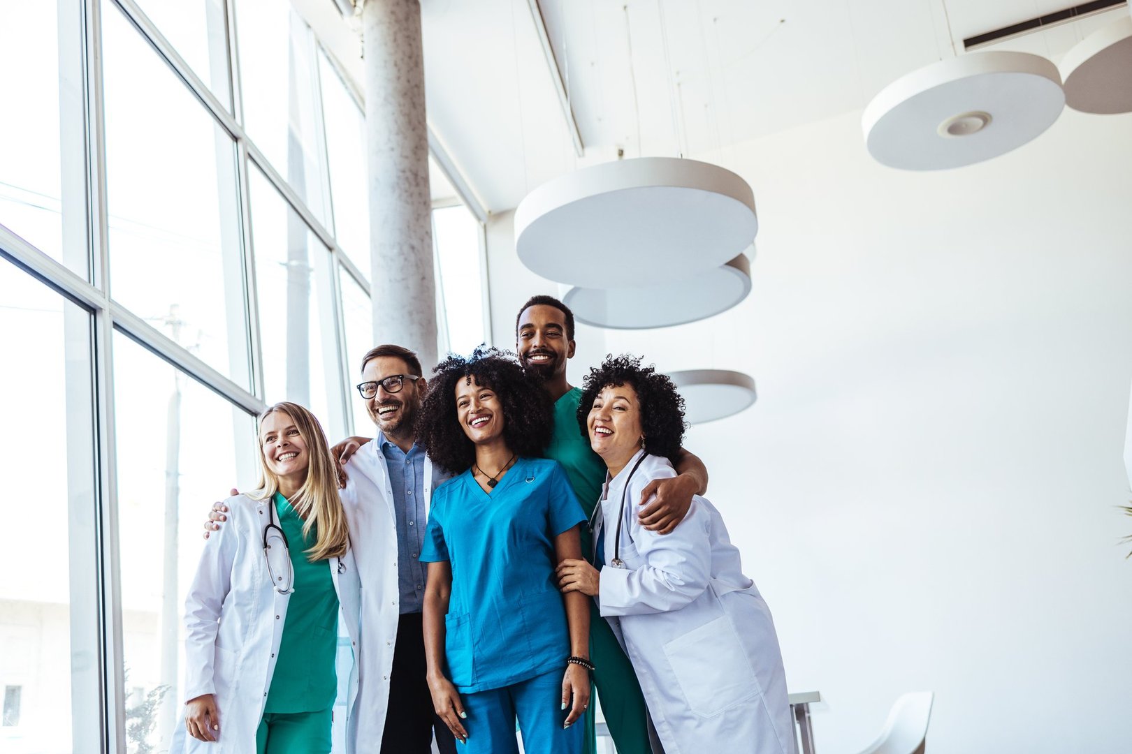 Diverse healthcare professionals in uniforms and lab coats showcase teamwork and unity within a bright contemporary setting, symbolizing cooperation, professionalism, and a positive work atmosphere.