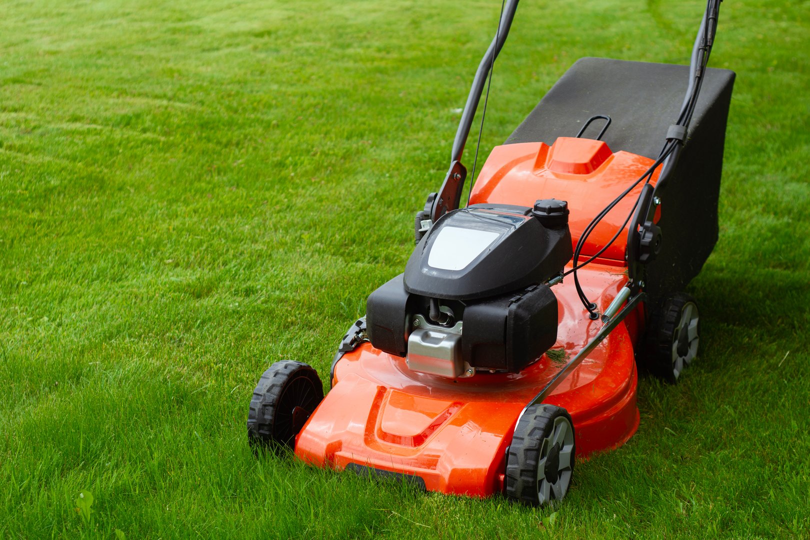 Bright orange lawn mower on lush green grass. Concept garden care, landscaping and summer outdoor work. Garden tool for lawn care and country lifestyle