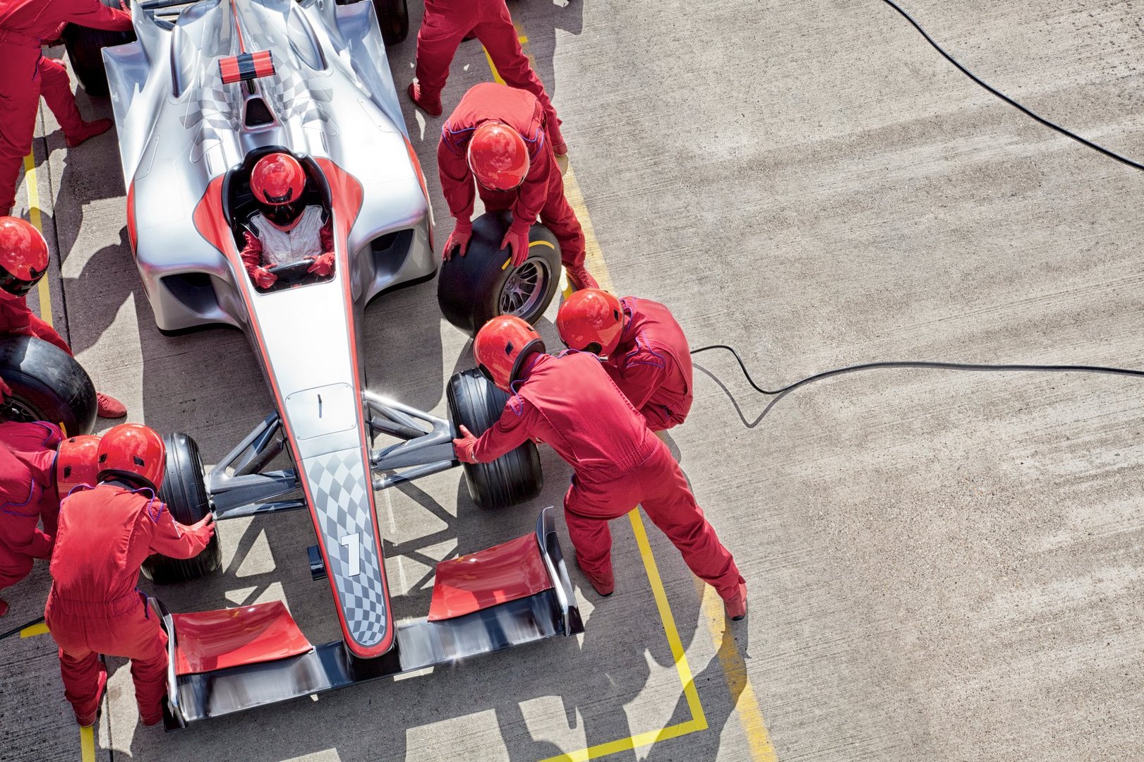 A race car undergoing a pit stop, with a team in red suits changing tires on a Formula 1 car on a racetrack.