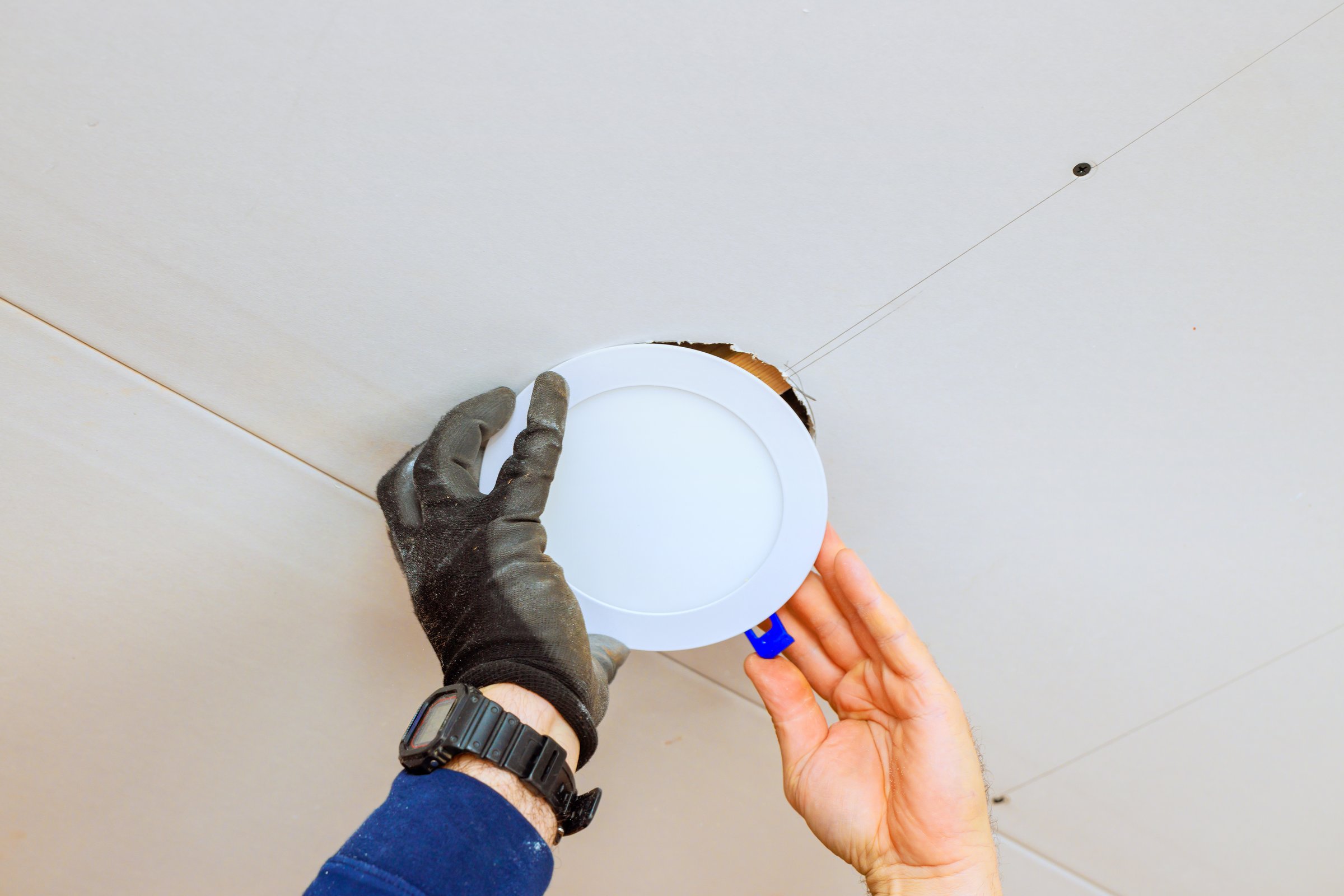 An electrician is carefully placing recessed light fixture into ceiling opening, during home renovation skills.
