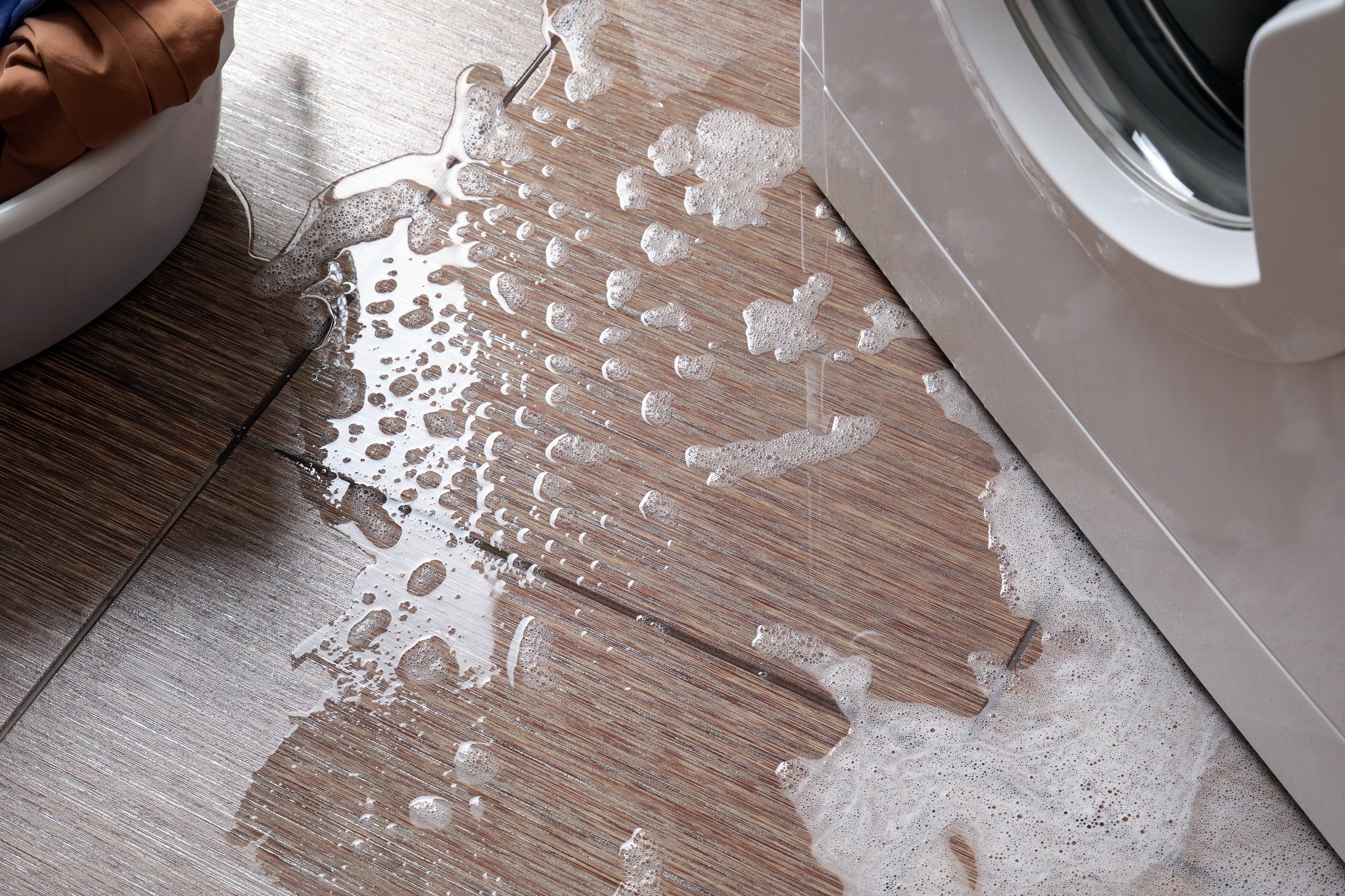 Breakdown of a household washing machine. Water with foam  out onto the floor from below.