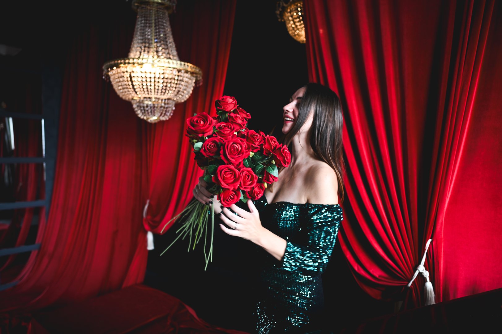 Young woman with red roses bouquet, enjoying the moment in a luxurious room with a crystal chandelier and red curtains