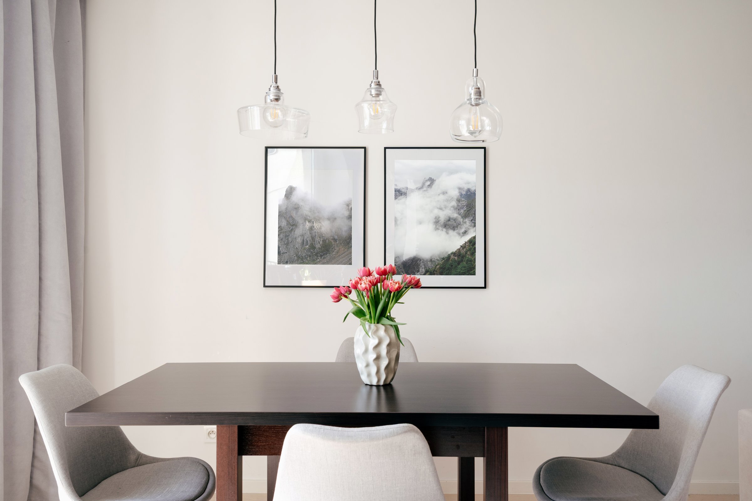 Dining area with black table surrounded by comfortable chairs. Pendant lights hang above desk with floral centerpiece. Minimalist design, home decor, picture frame in room