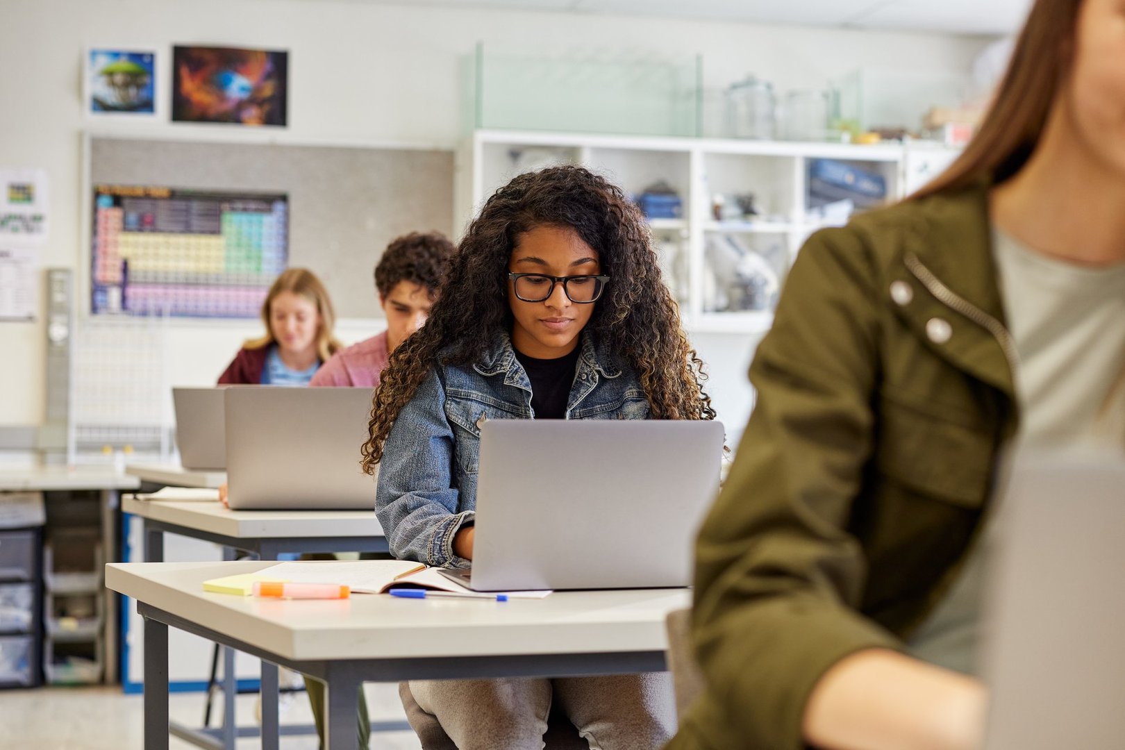 Serious multiethnic girl student wearing eyeglasses while working on laptop in a classroom with copy space. Focused african american girl typing on laptop with study material on desk. Guys and girls using laptop during computer lesson in secondary classroom.