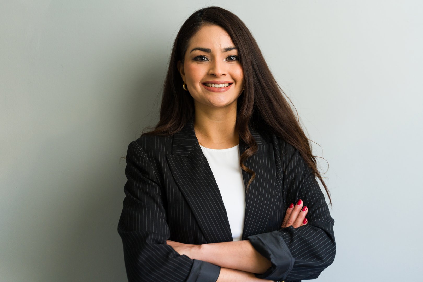 Portrait of a cheerful businesswoman wearing a suit with folded arms, exuding confidence and professionalism in a corporate setting