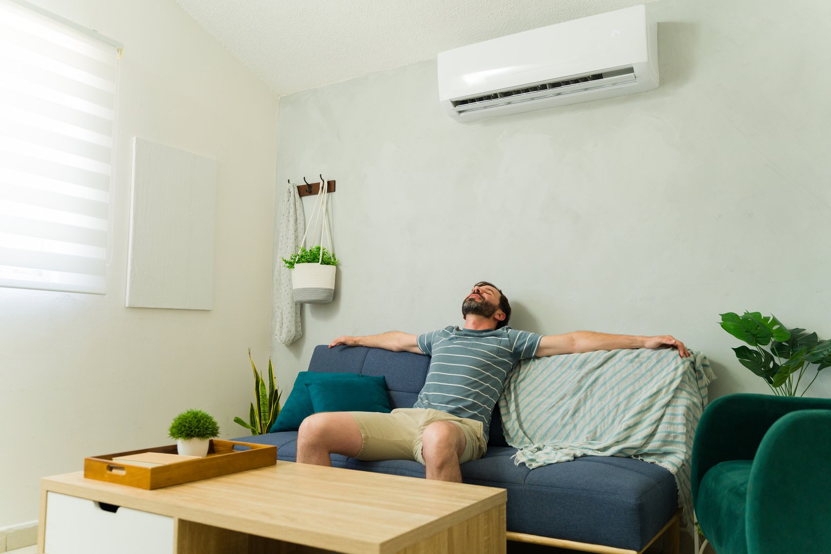 Man lounging on a sofa at home, savoring the refreshing coolness of air conditioning during the sweltering summer heat