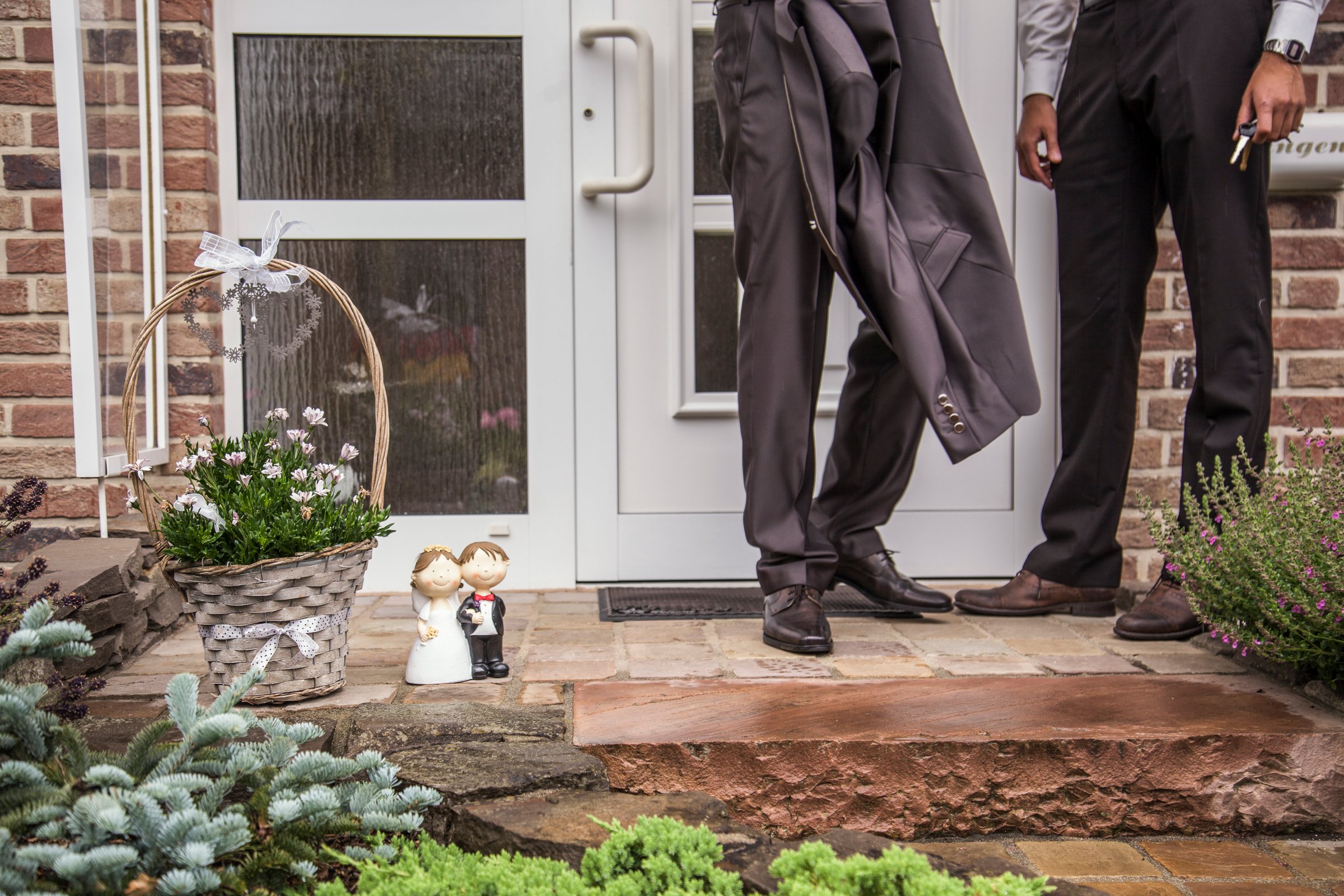 A groom is seen adjusting his suit while standing in front of a wedding venue. Decorative elements and floral arrangements enhance the atmosphere as guests anticipate the ceremony's start.