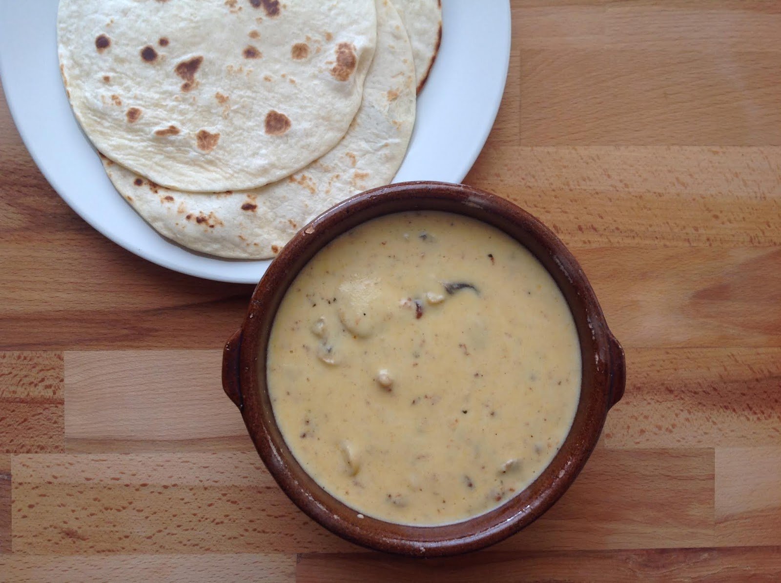 Bowl of creamy soup with mushrooms next to a plate of flour tortillas on a wooden table.