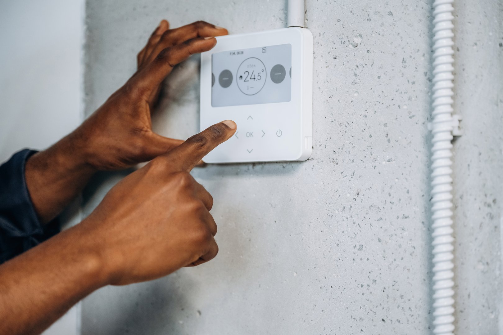 Thermostat on the wall. The repairman's hands fix it.