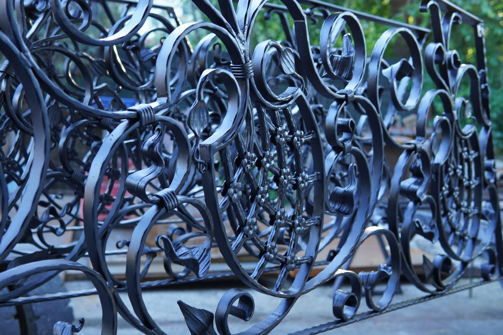 Close up of a decorative wrought iron fence. Wrought iron fence with intricate swirls, leaf motifs. This metal fence is handcrafted and finished in an elegant matte black powder coat