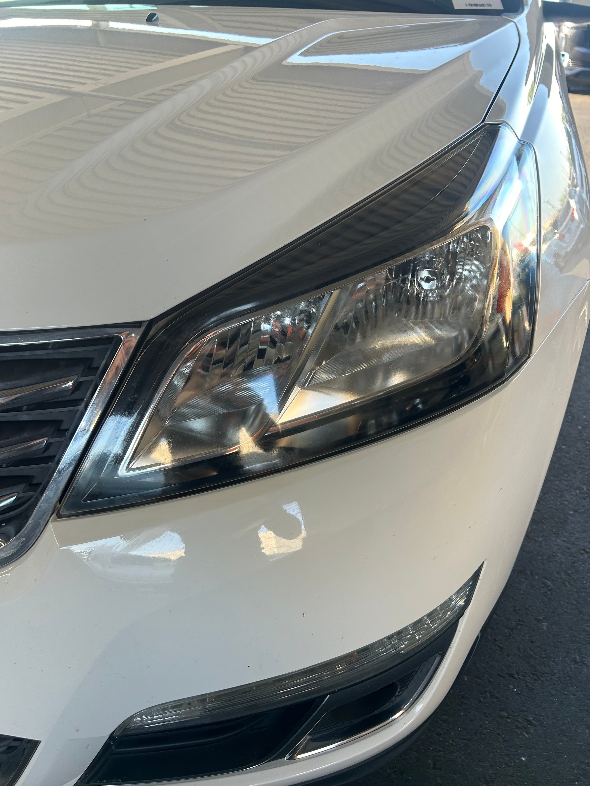 Close-up of a car's front headlight, showcasing the vehicle's sleek white exterior and detailed light design.