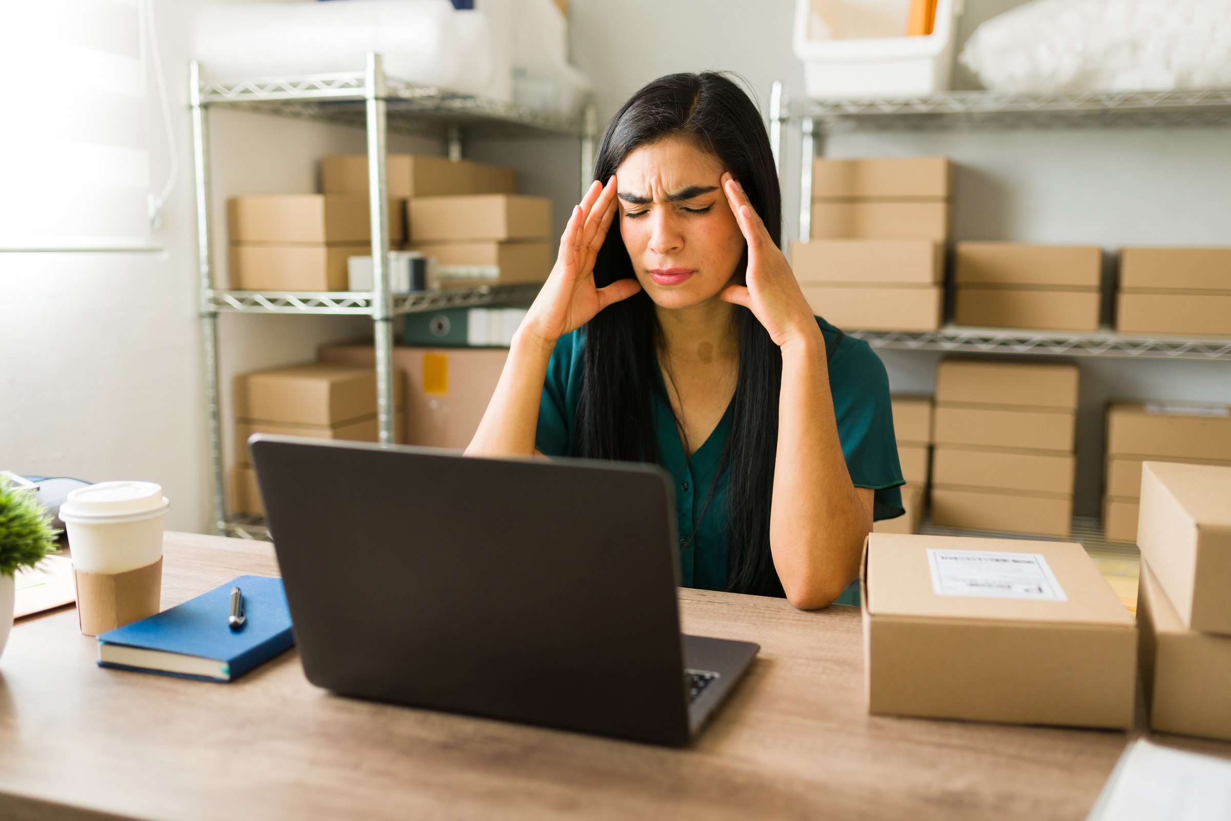 Female latin entrepreneur experiencing a headache while working on her laptop in her online store office and managing her small business