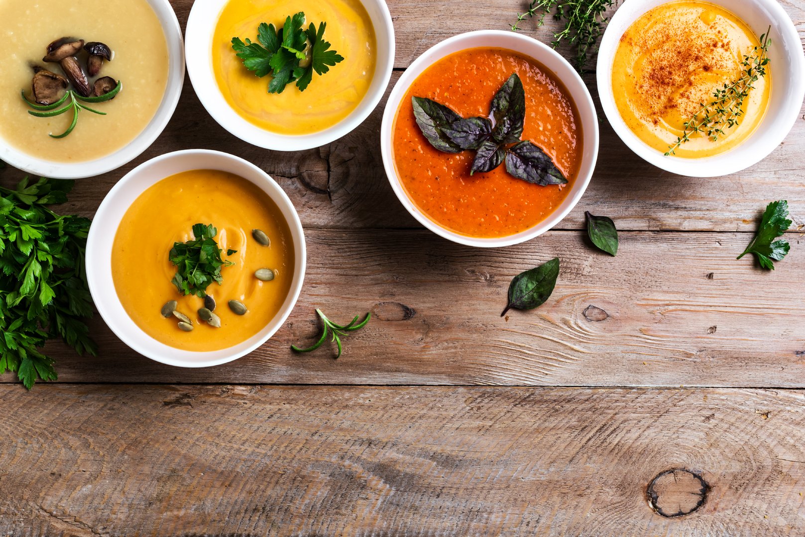 Autumn soups. Set of various seasonal vegetable soups and organic ingredients on wooden background, top view, copy space. Homemade colourful seasonal vegan soups.
