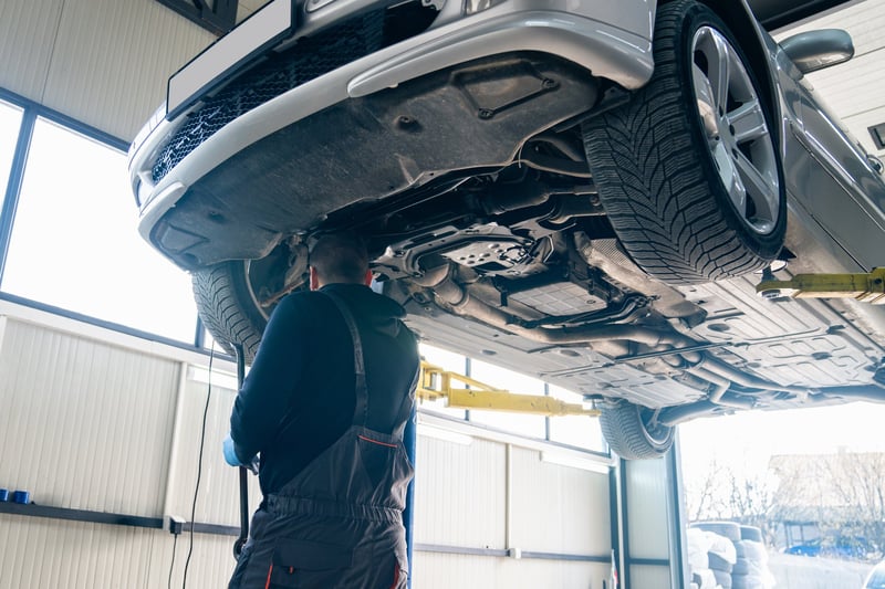 Serviceman checks car suspension on a column lift in car service.