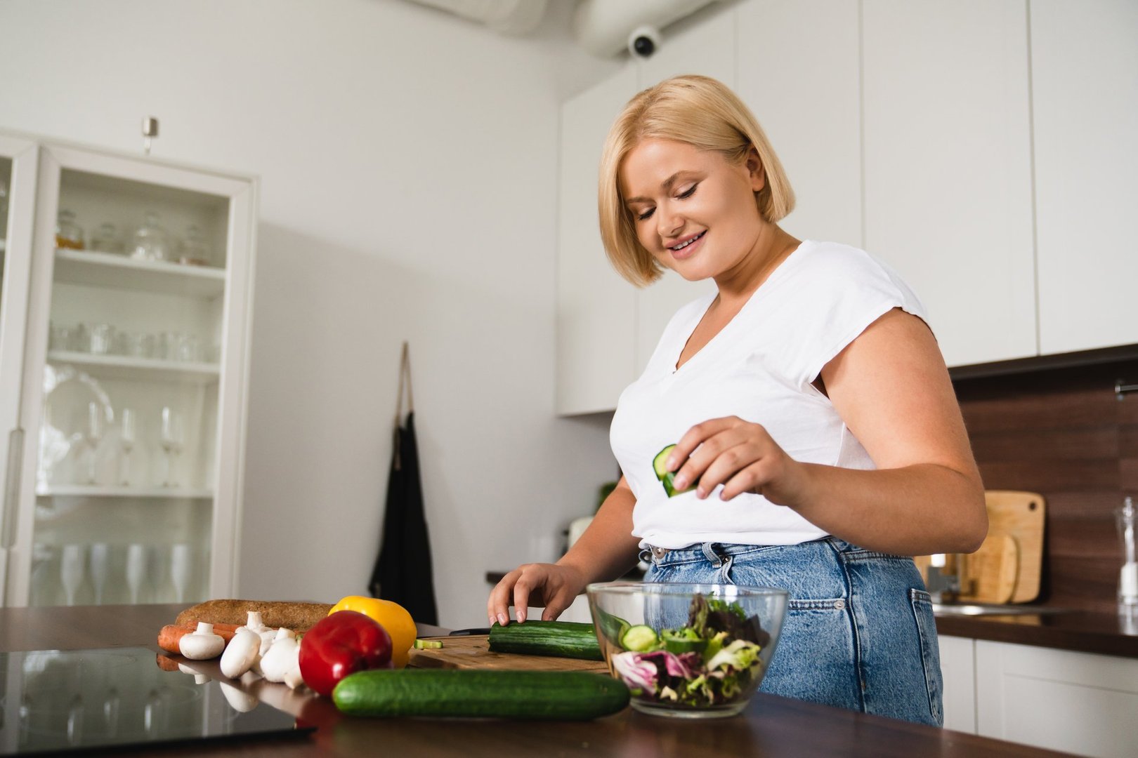 Young caucasian plump plus size woman cooking making salad, healthy food, dieting, counting calories, preparing dinner lunch at home kitchen