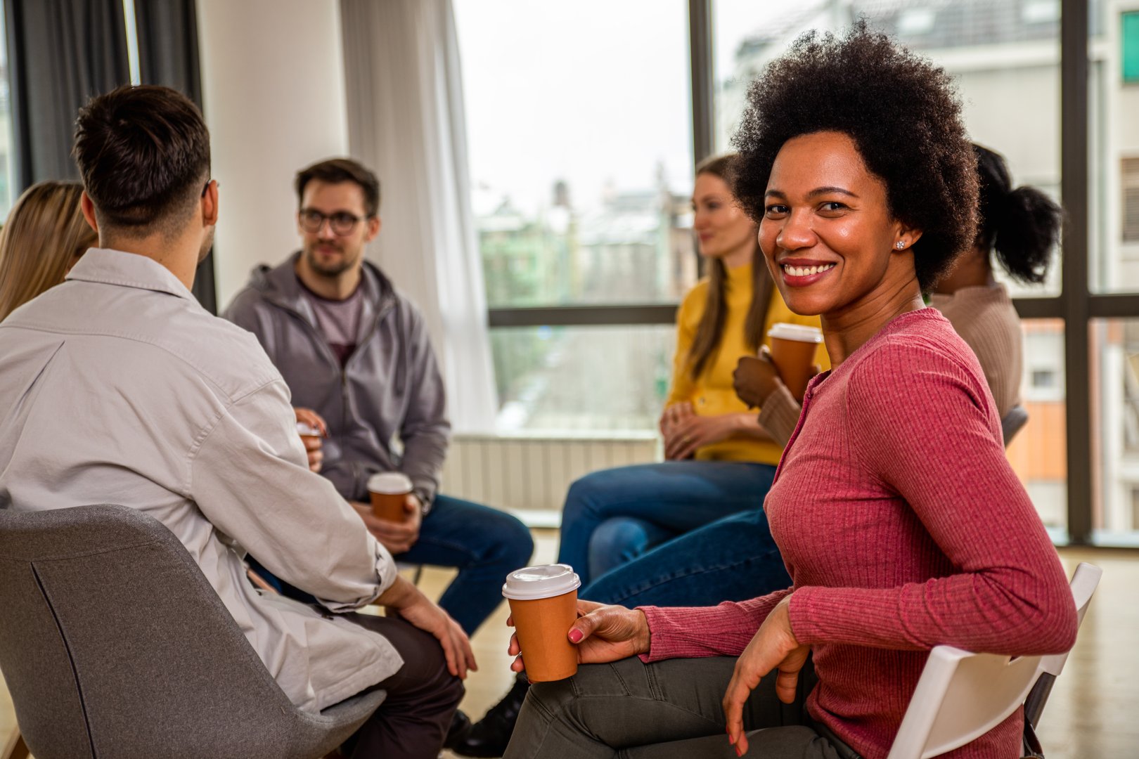 Portrait of a woman with diverse group of people sitting in circle in group therapy session.