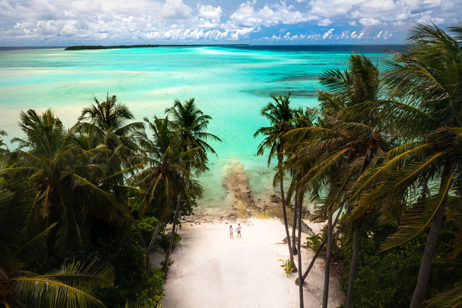 Couple walking hand in hand on pristine white sand beach surrounded by palm trees and turquoise waters in Maldives