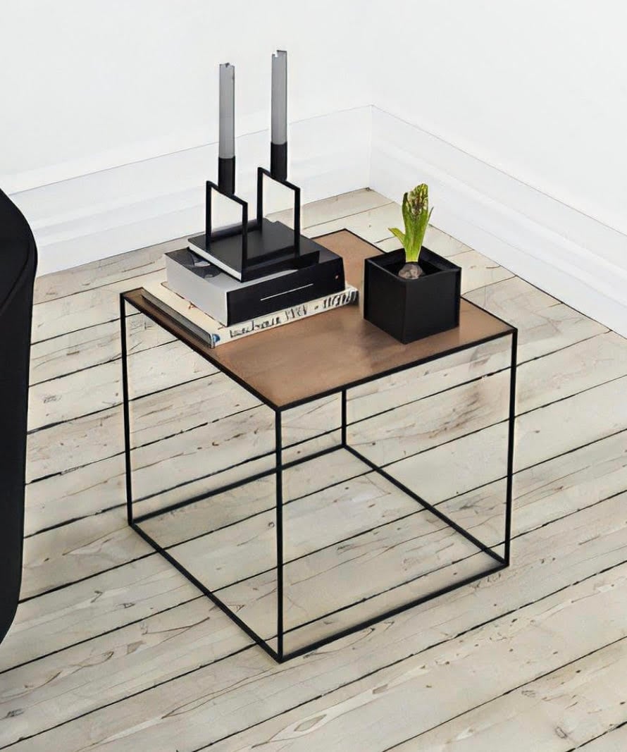 Modern side table with a metal frame, wooden top, books, candle holders, and a small plant on a light wood floor.