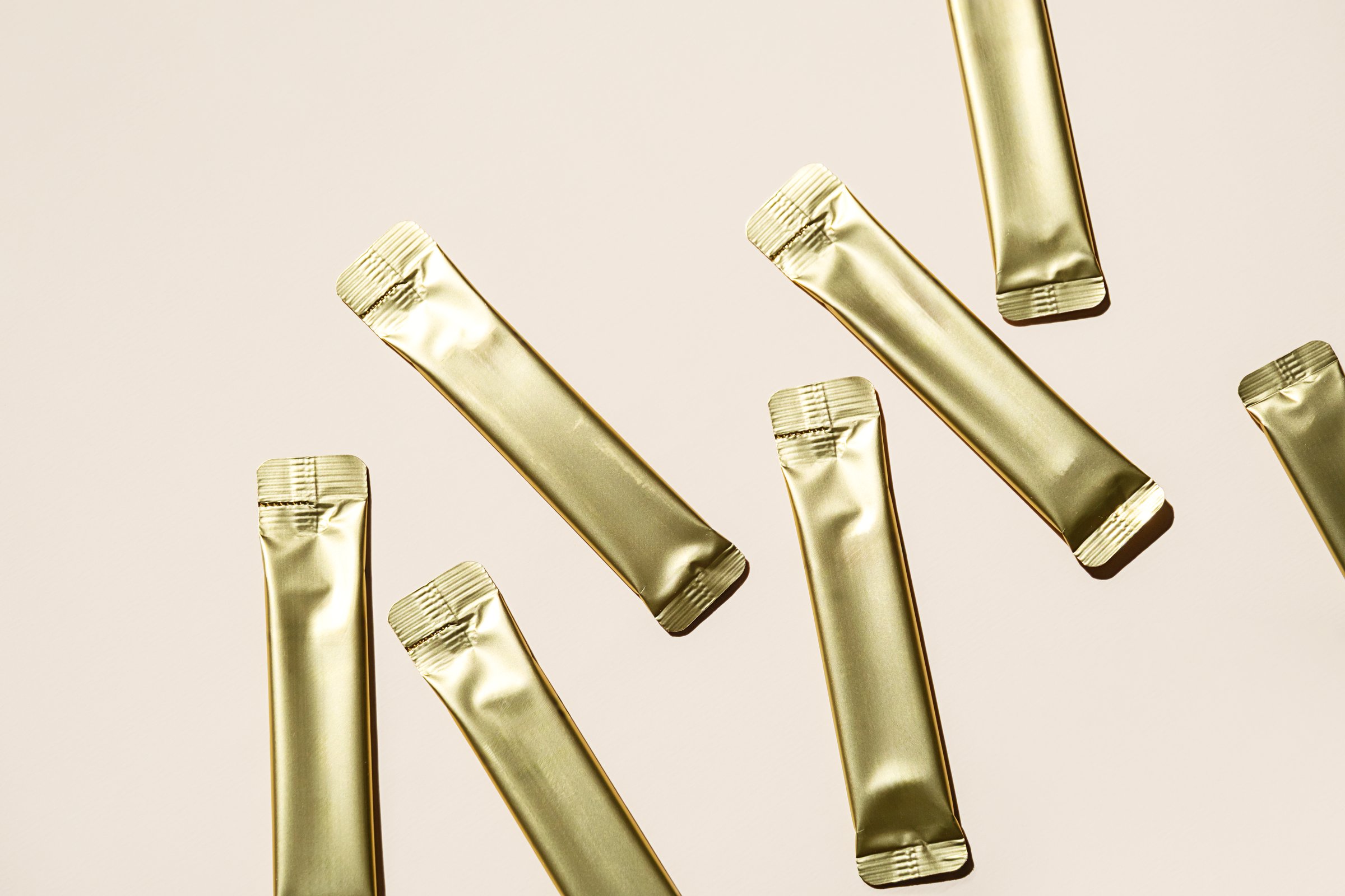 Several Golden Stick Packaging Sachets on Light Background. Unbranded Foil Pouch Mockup for Product Presentation.