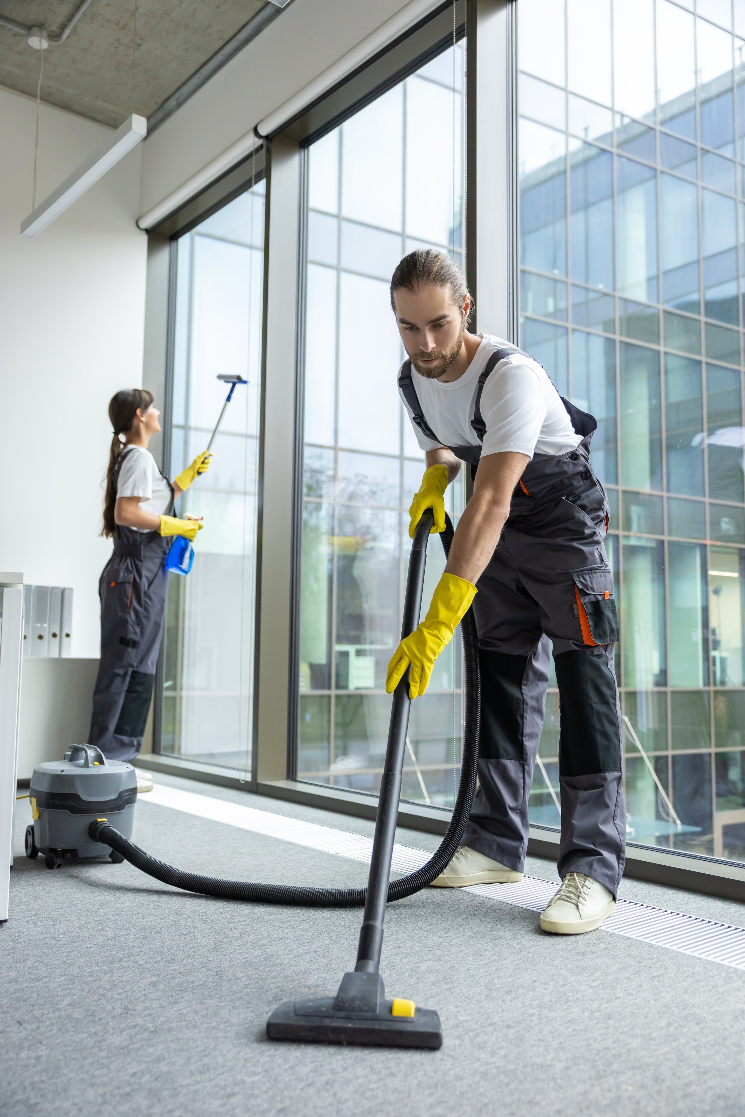 Vacuum cleaning. Young man in uniform vacuum cleaning the floor in the conference room