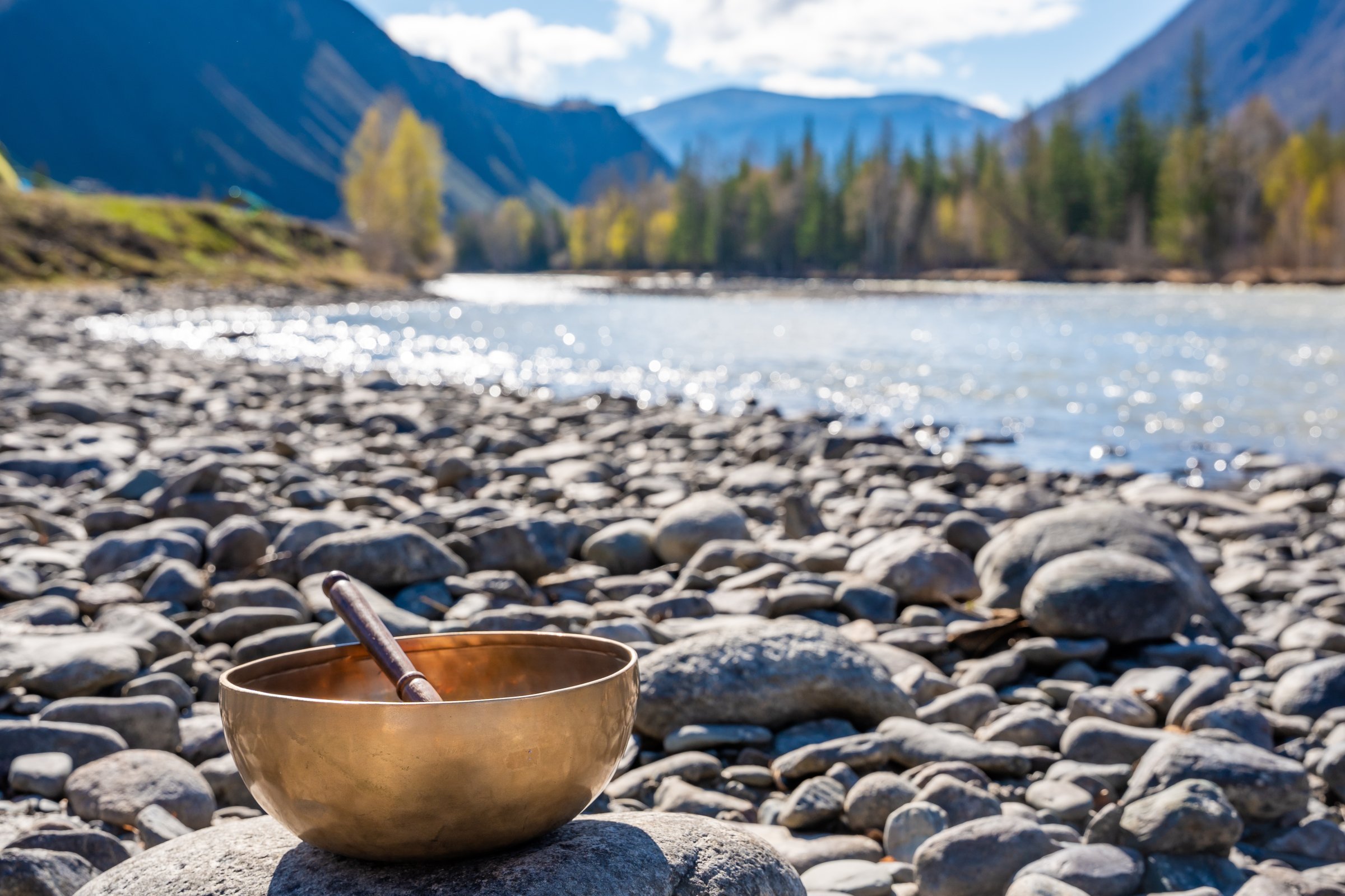 Tibetan singing bowl placed on river stones near mountain water in Altai. Concept of grounding energy, sacred silence, and spiritual resonance in wild nature. High quality photo