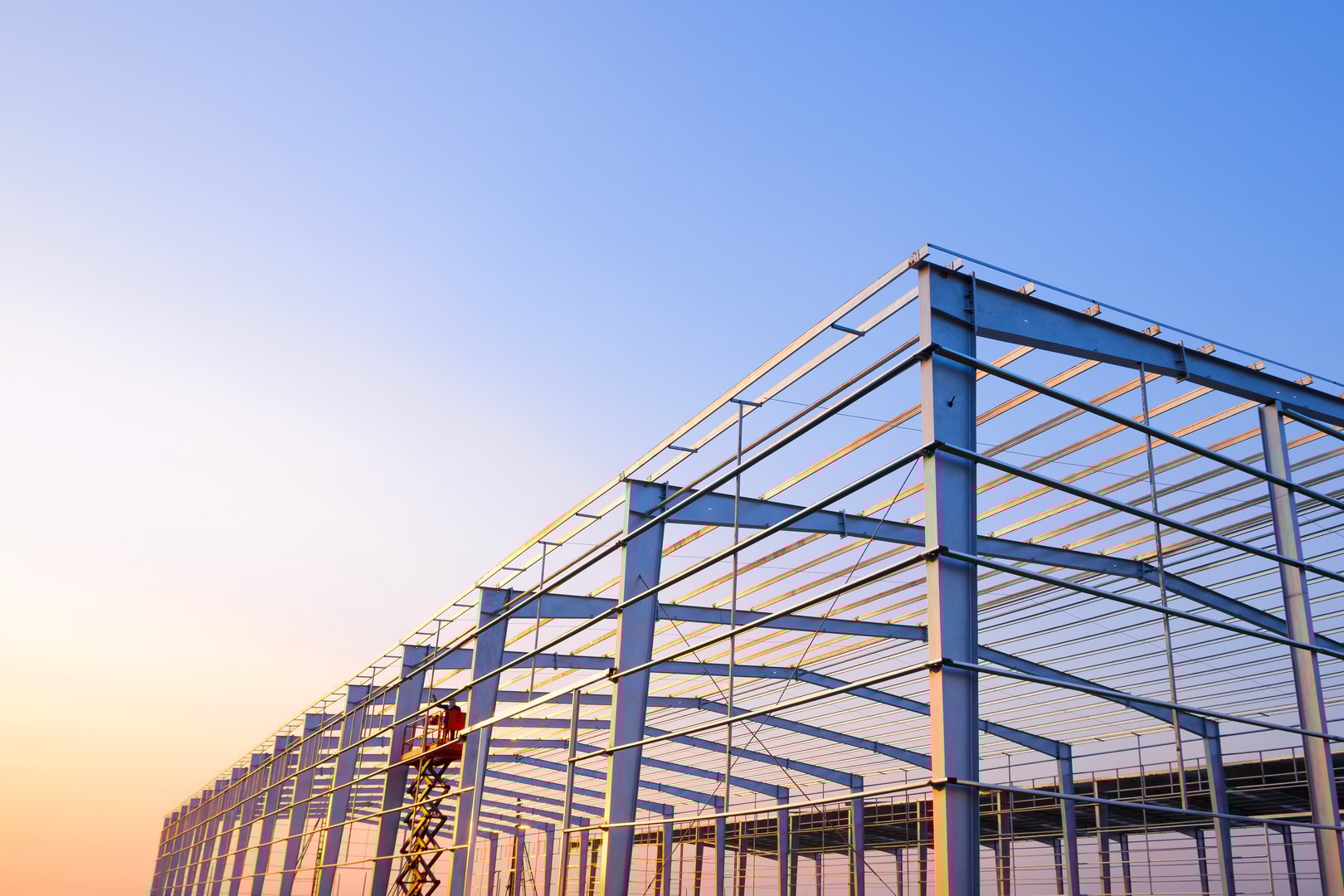 Metal posts and roof beam structure of factory industrial building framework in construction site against sunset sky background, Low angle and perspective side view