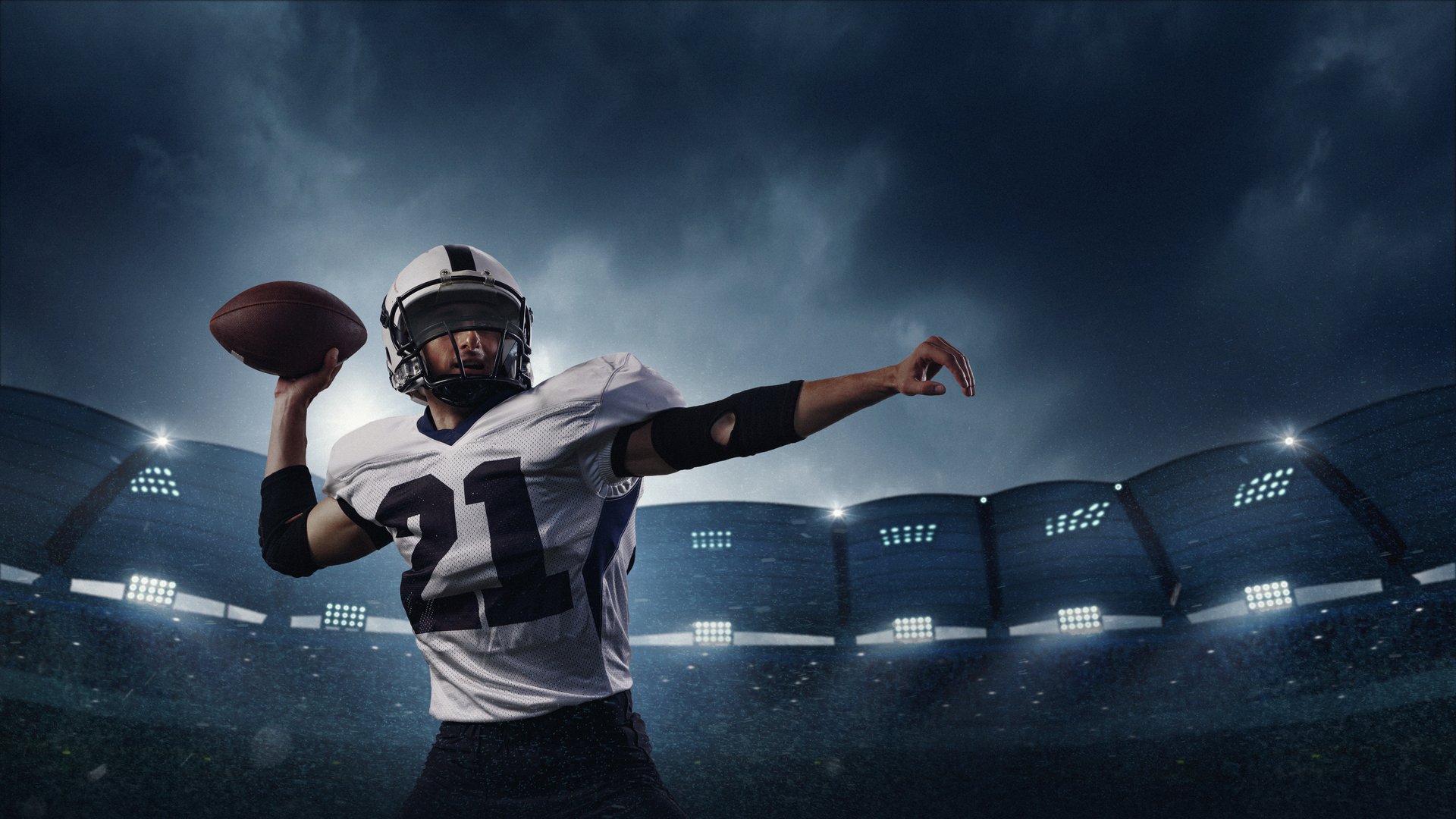 Focused American football quarterback in white jersey prepares to throw football during night game under dramatic stadium lighting. Concept of sports marketing and branding.