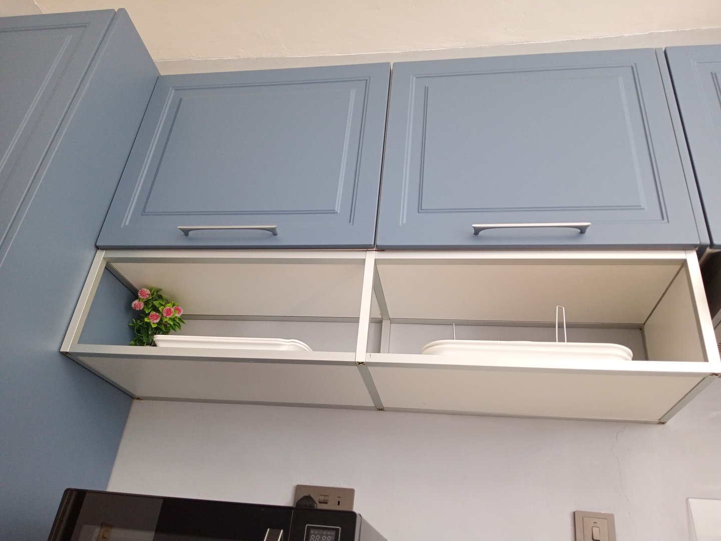 Overhead kitchen cabinets with open drawers, showing a small potted plant and food storage containers inside.