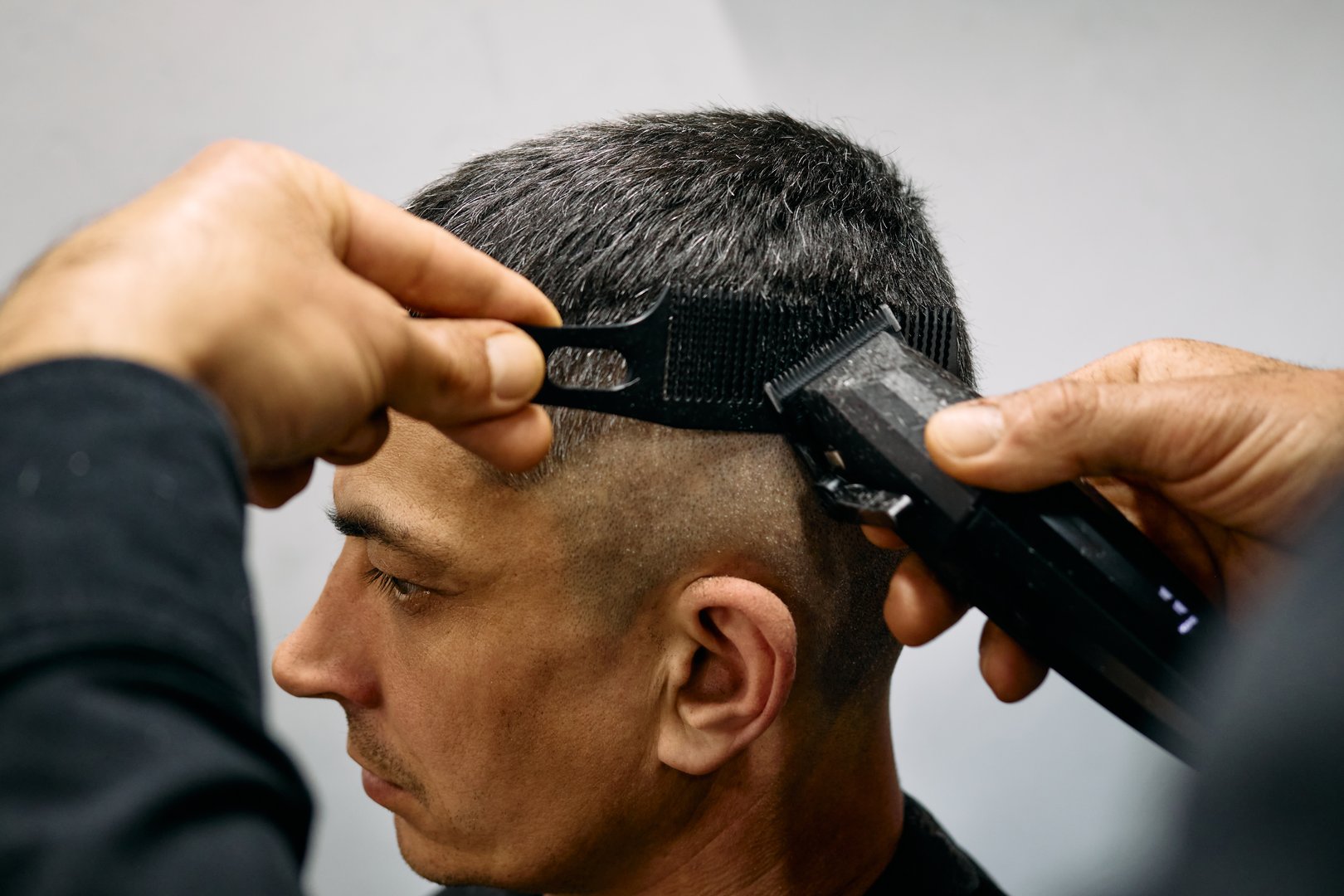 A skilled barber uses clippers to craft a well-defined haircut while ensuring the customer's hairstyle remains stylish and clean. The atmosphere is vibrant, reflecting a trendy barbershop environment.