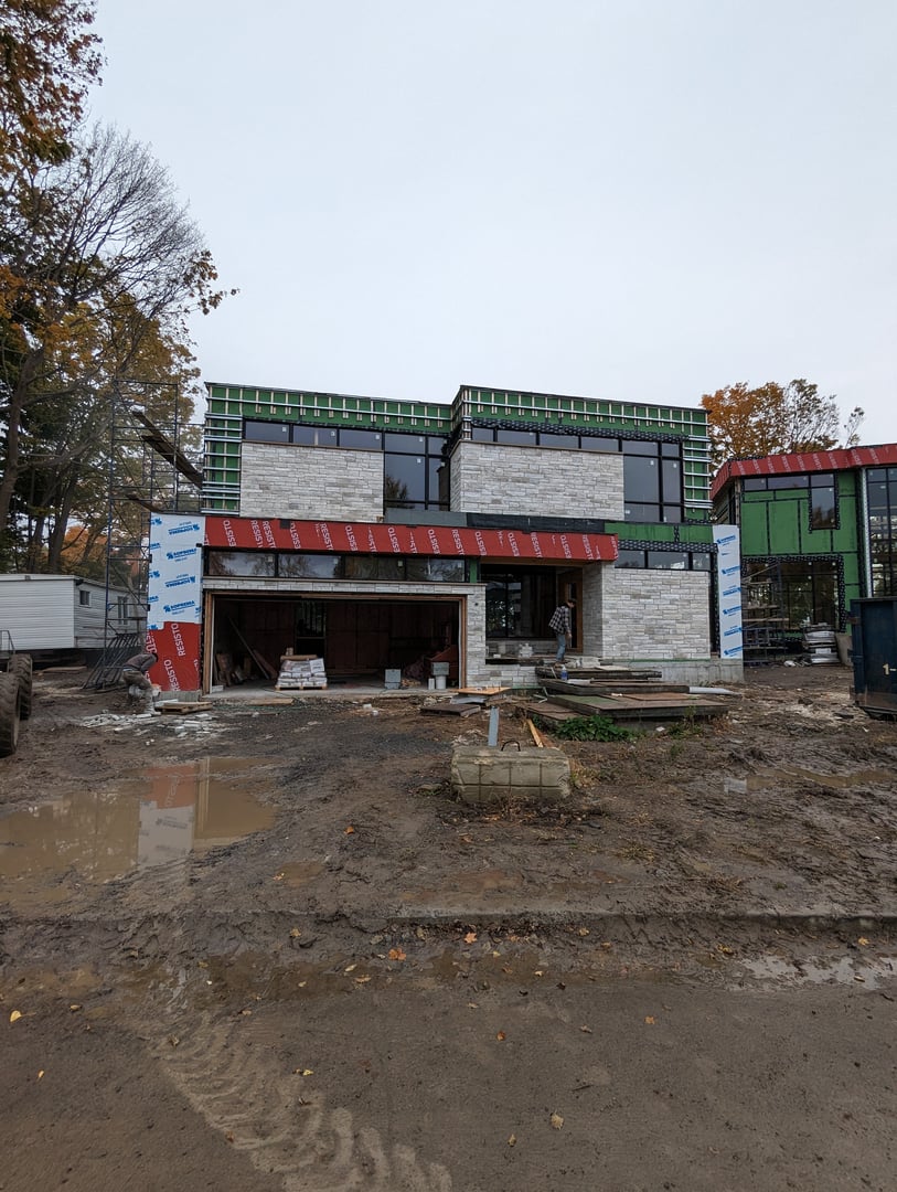 A modern house under construction with exposed walls and scaffolding, surrounded by mud and construction materials.
