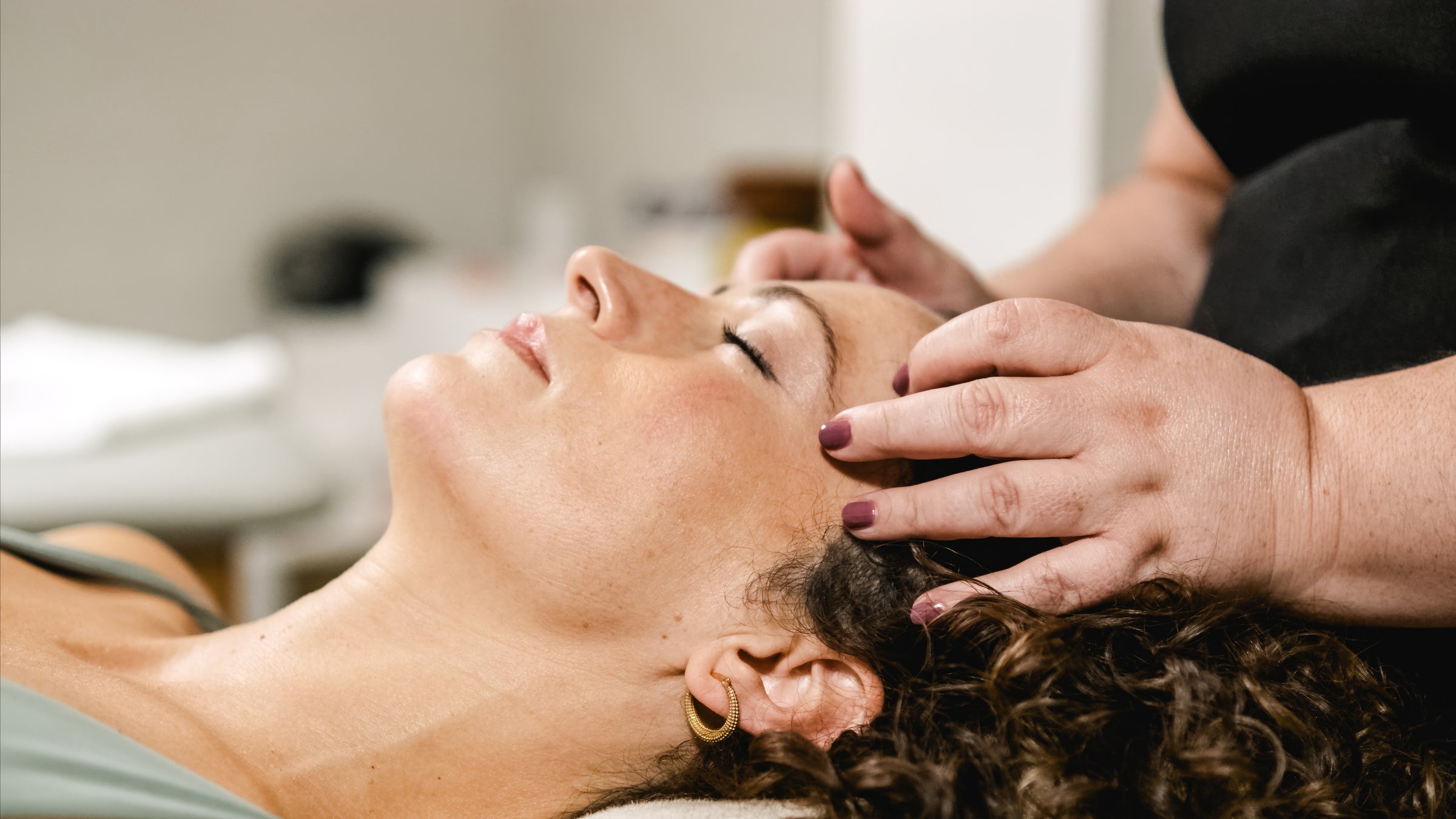 Masseuse giving relaxing head massage to client lying on massage table in spa salon