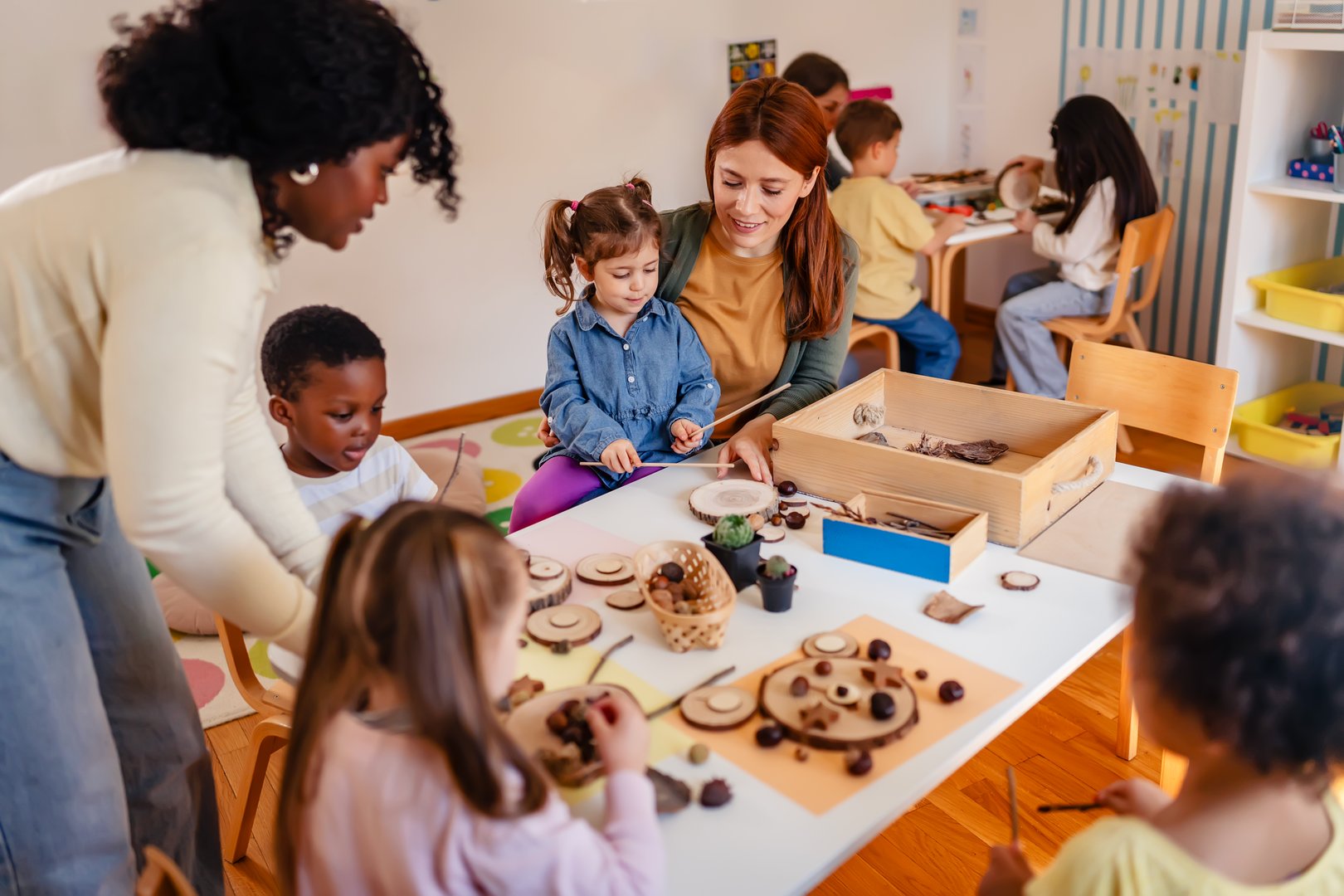 Preschool teacher guides a diverse group of children in a natural materials activity in a bright, creative classroom setting focused on hands-on learning.