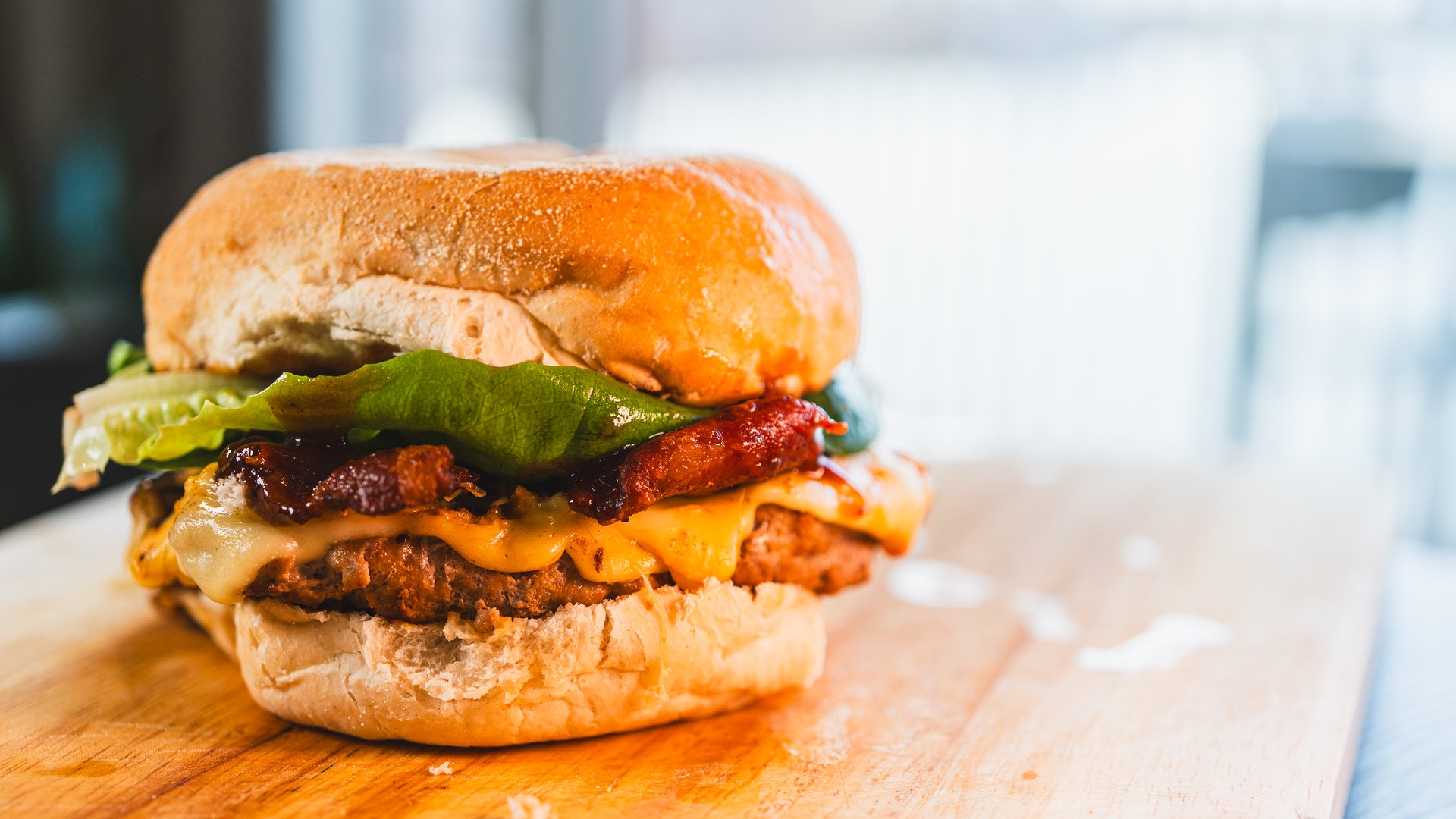 A perfectly grilled, juicy single-patty burger topped with crispy bacon, abundant melted cheese, and fresh green lettuce. A classic and delicious gourmet meal, captured in all its glory.