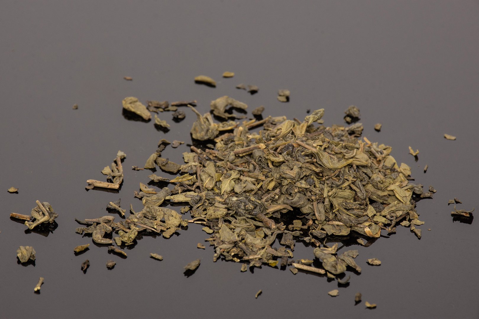 Lot of pieces of dry green tea on black glass