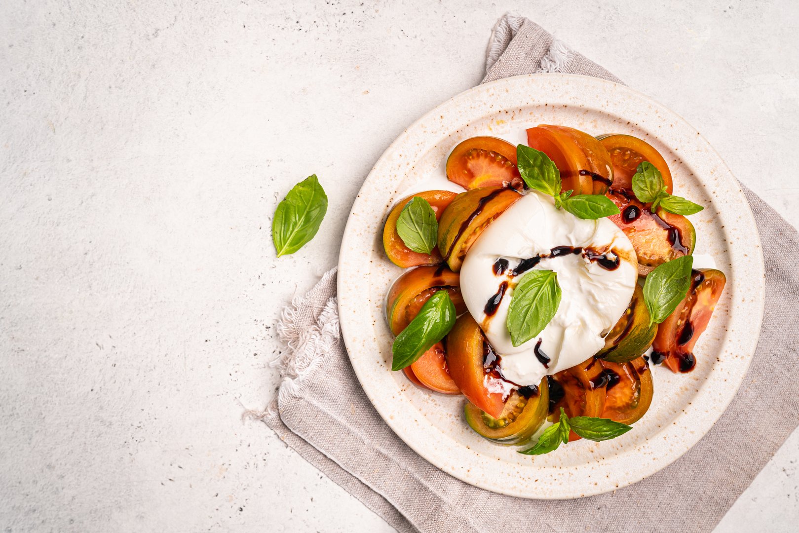 Caprese salad with burrata cheese, tomato, basil and balsamic vinegar arranged on white plate, on white background top view. High quality photo