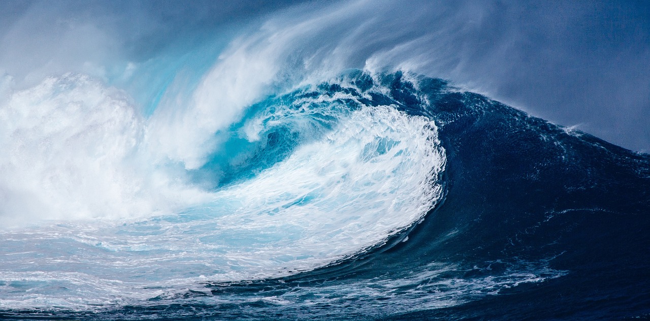 Massive ocean wave crashing with white foam under a clear blue sky.