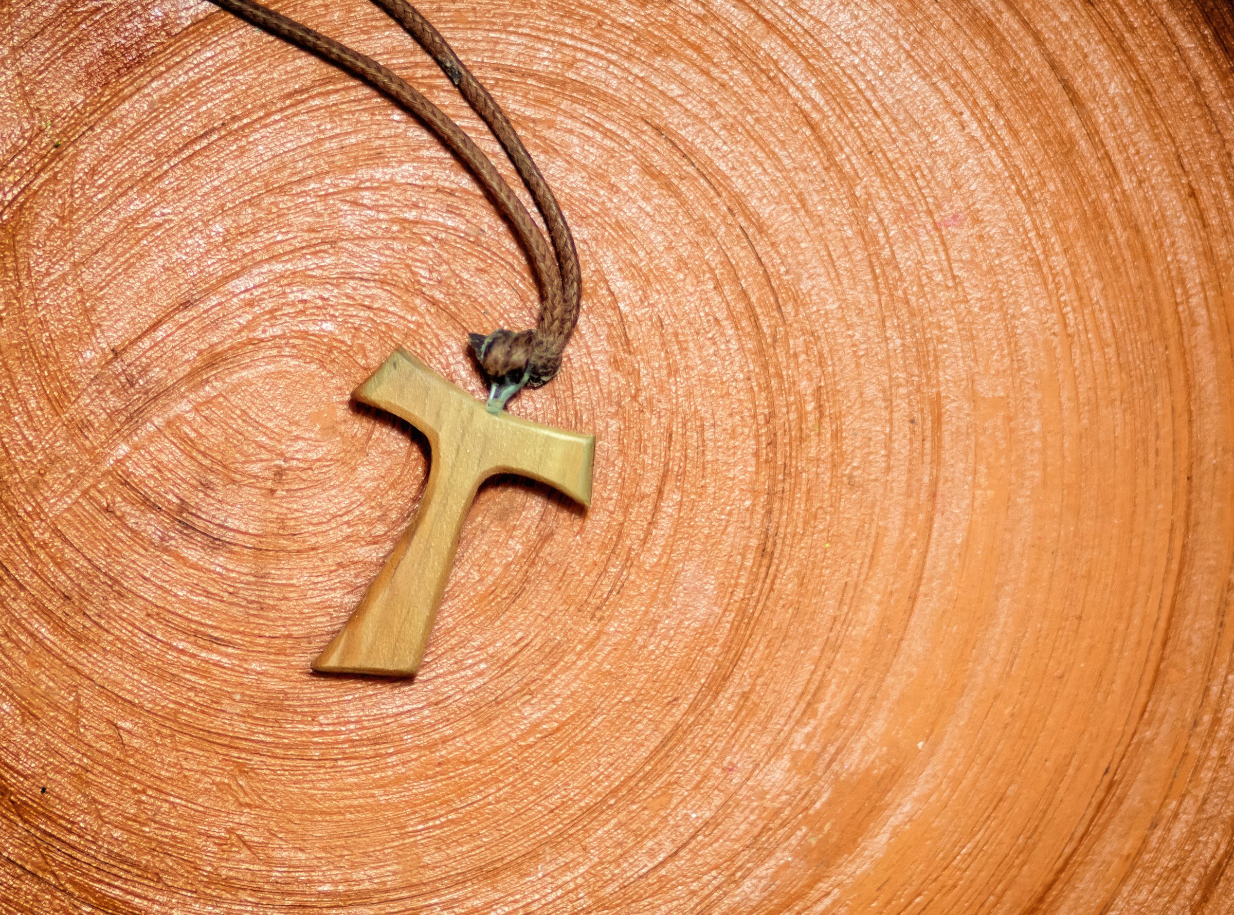 Wooden tau cross pendant featuring a brown cord, resting gracefully on a terracotta surface, symbolizing faith, Christianity, and deeper spiritual meanings