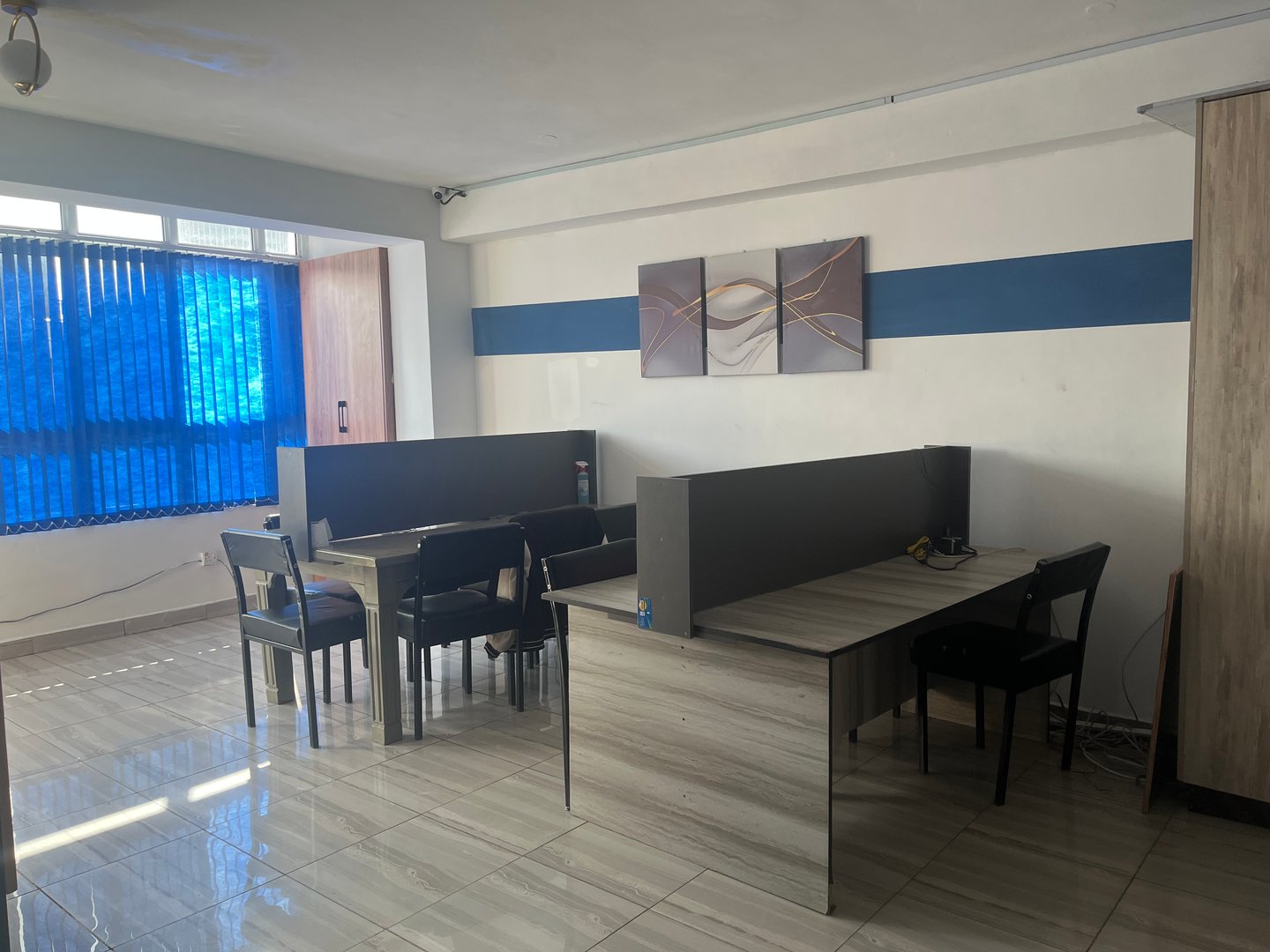 Modern office space with partitioned desks, chairs, abstract wall art, and blue window blinds.