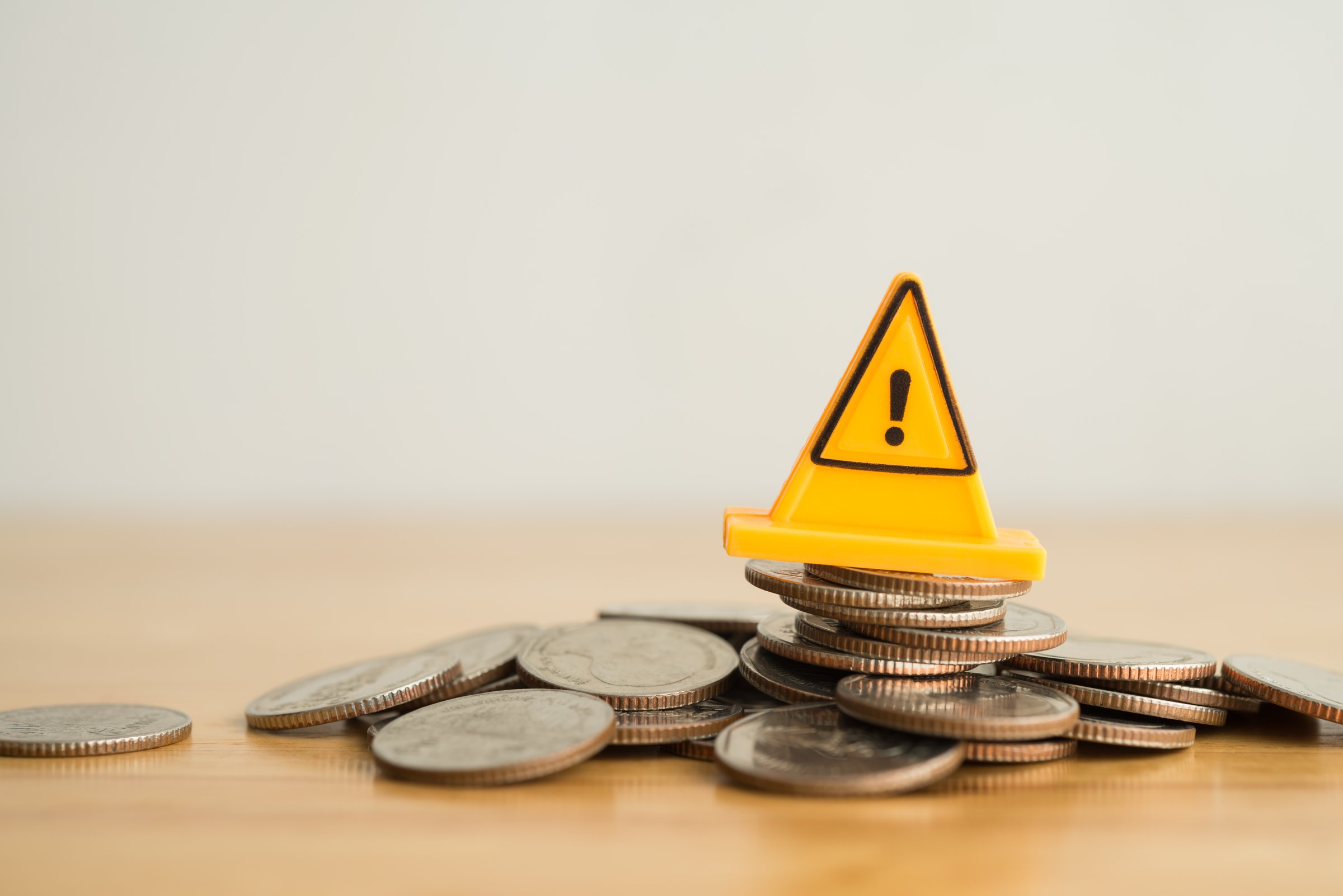 Yellow warning sign label on stack coins crash on wooden table with white background copy space. Risk and financial management in business, economy crisis, stock market investment, banking concept.