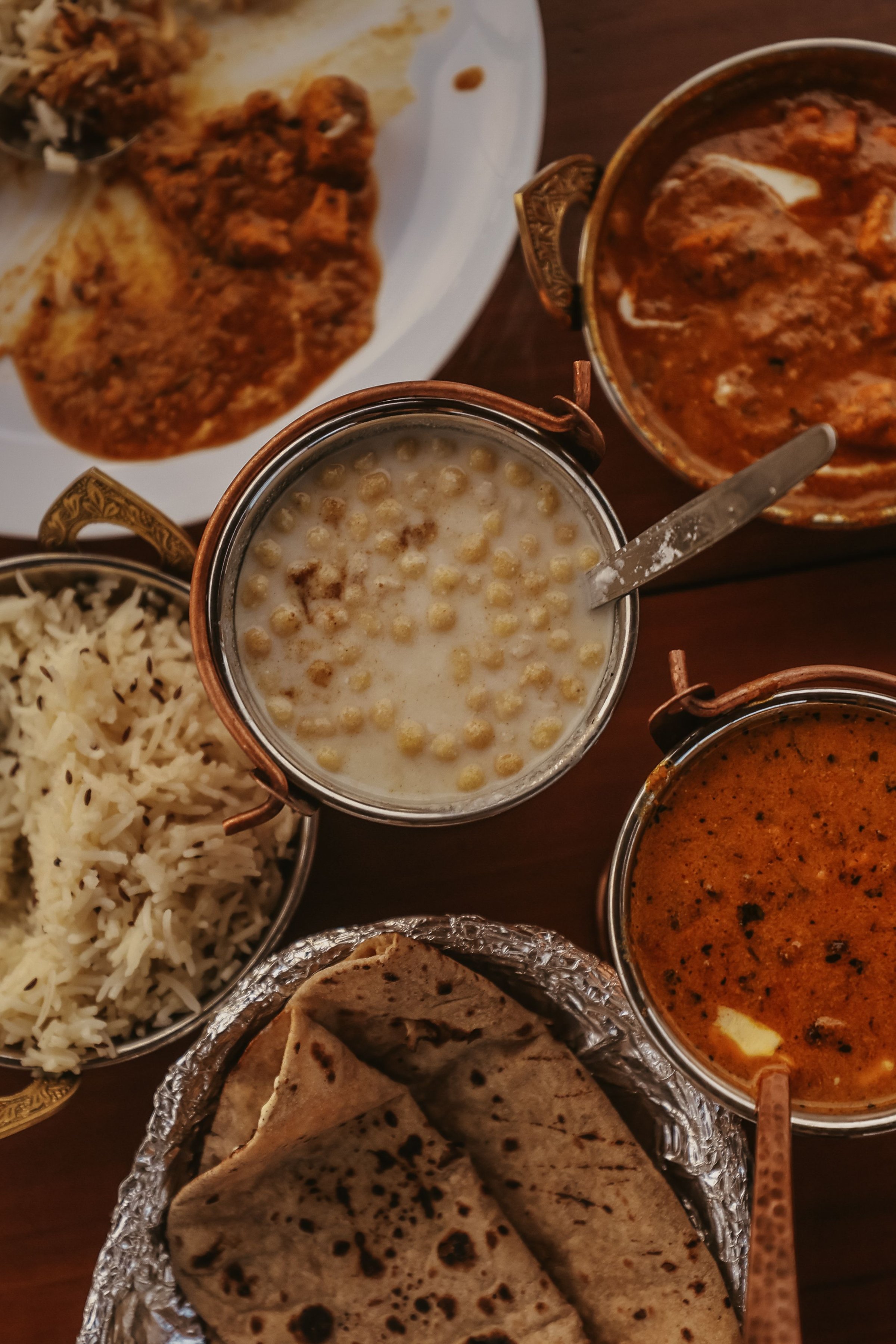 A traditional Indian meal with curry, rice, naan, and dessert in ornate bowls on a wooden table