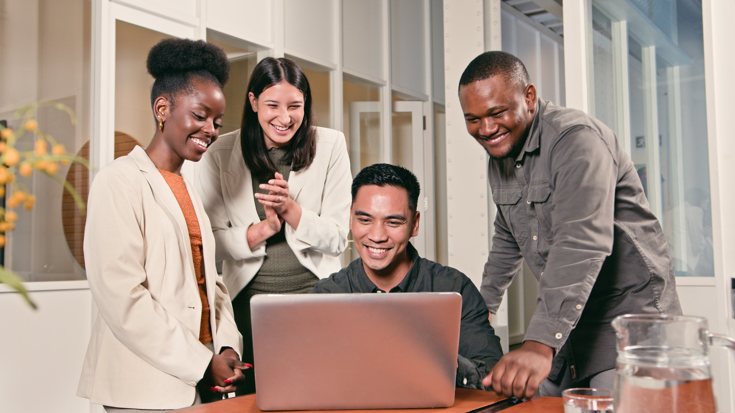 A diverse group of professionals gathered around a laptop, engaging in a collaborative effort within a modern workspace. The atmosphere reflects teamwork, cooperation, and productivity in a business environment.