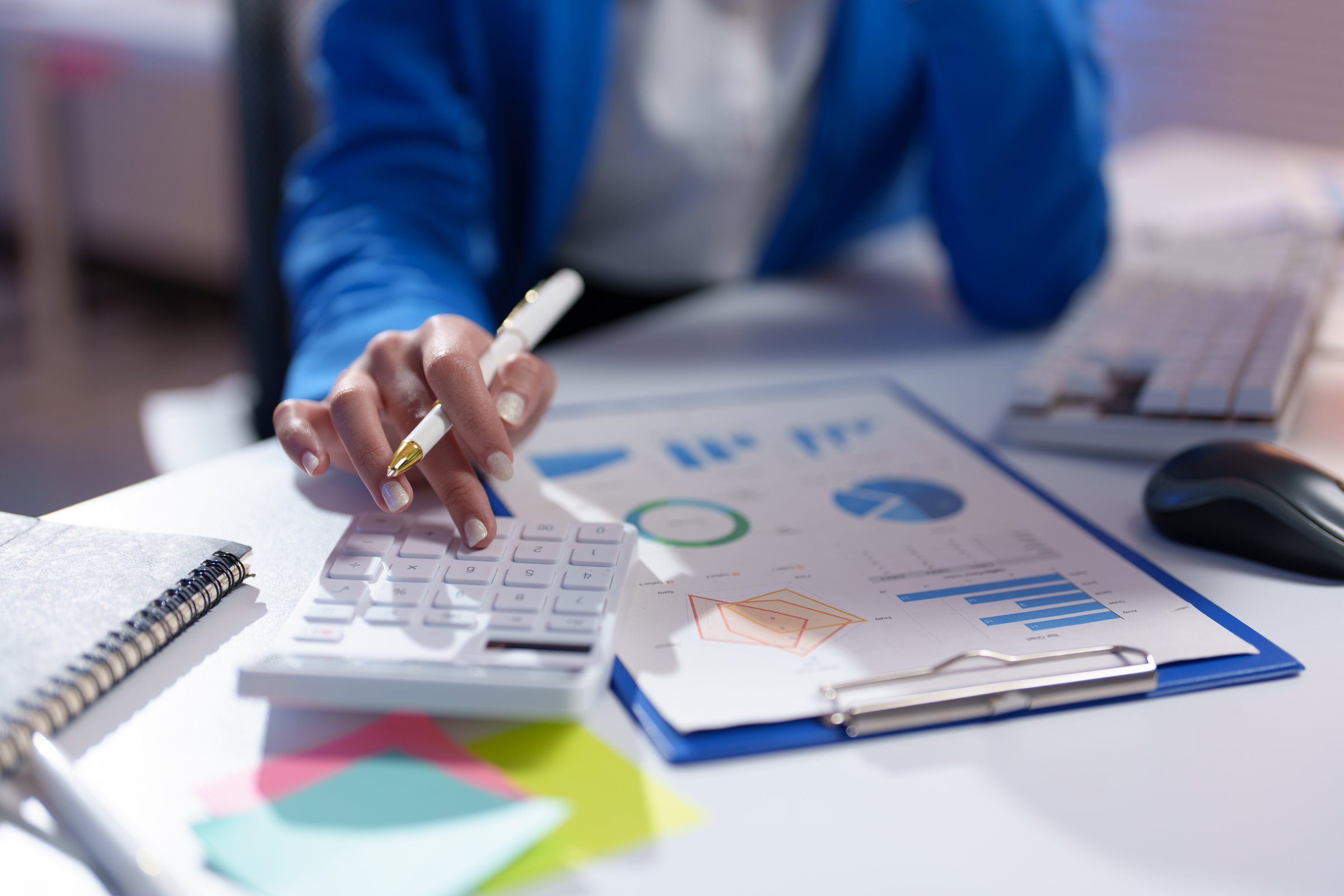 Close-up of a businesswoman's hands using a calculator and analyzing financial charts, showcasing data analysis and financial planning in a professional setting