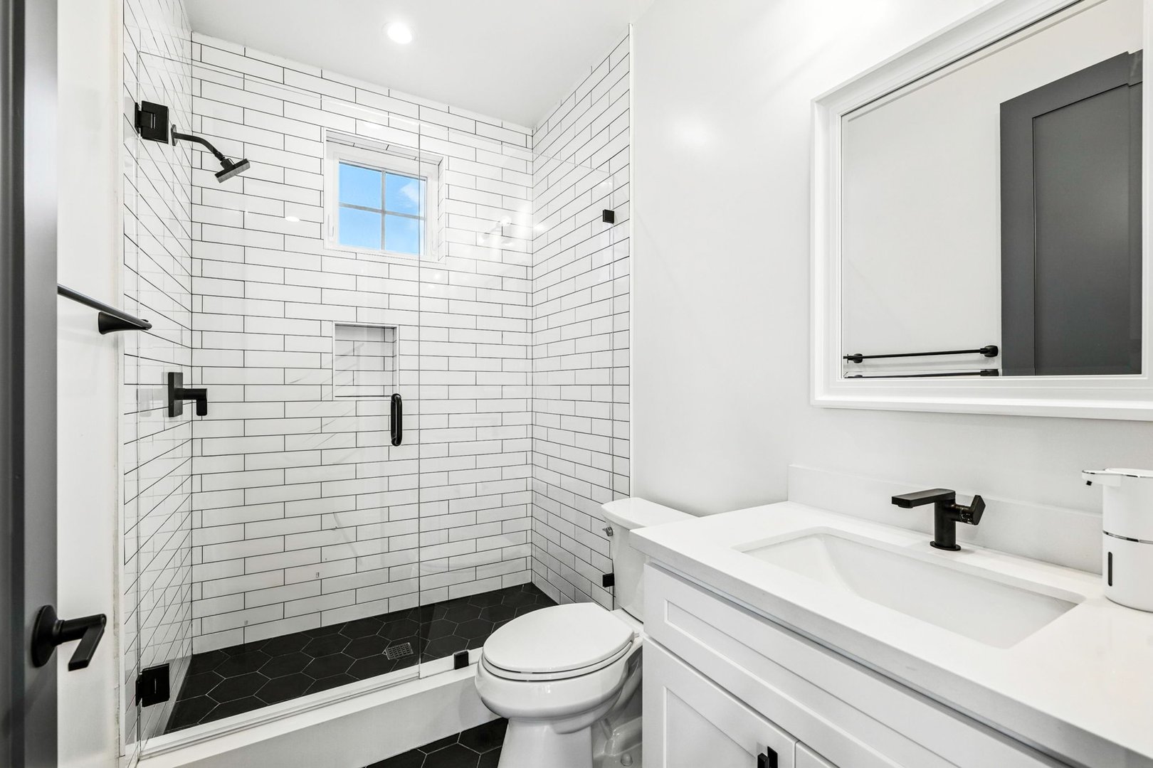 Modern white bathroom with subway tiles, black fixtures, and a glass shower door, featuring a sleek vanity and mirror.
