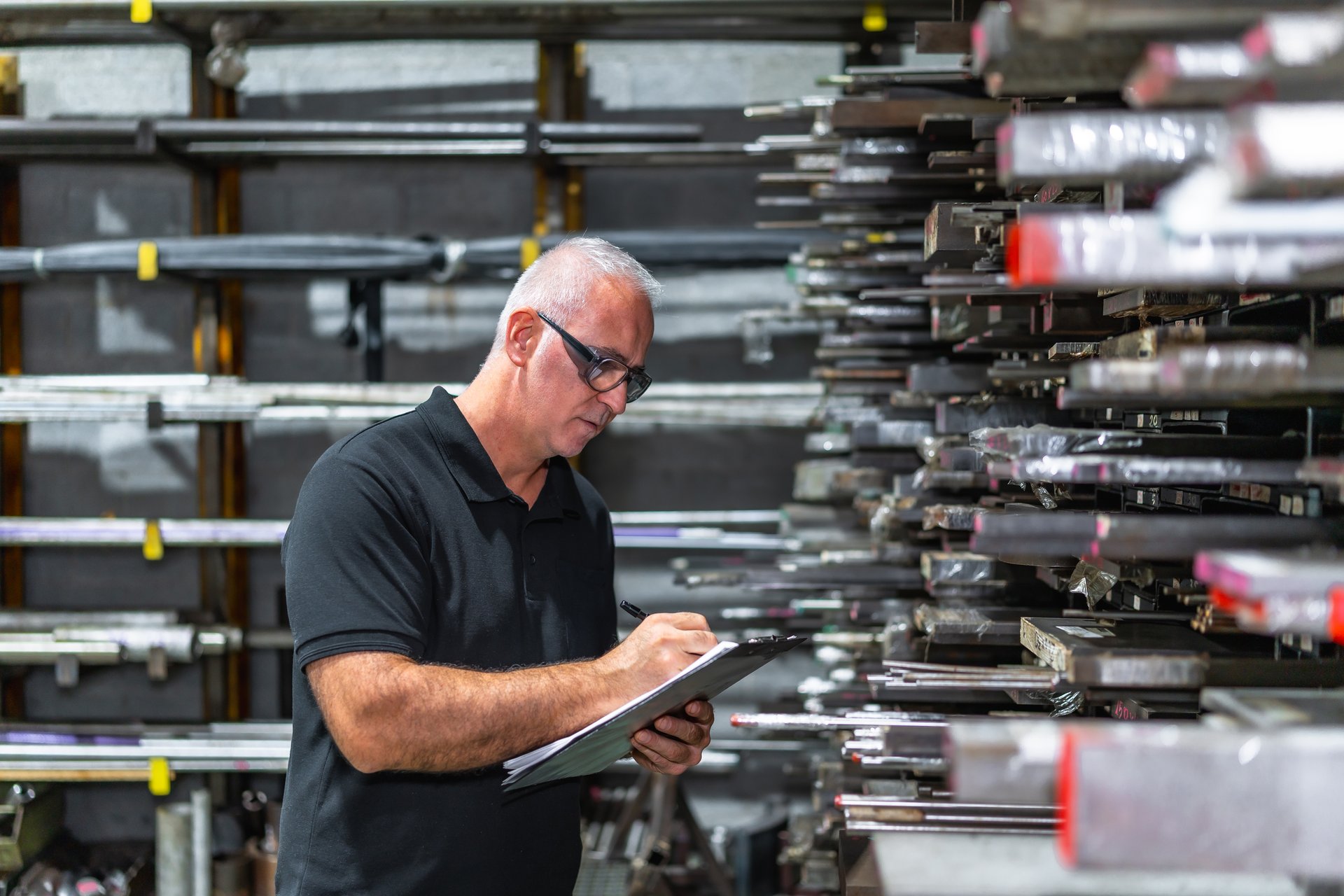 Side view photo of a mature caucasian man checking metal bars while doing inventory using a clipboard in a factory