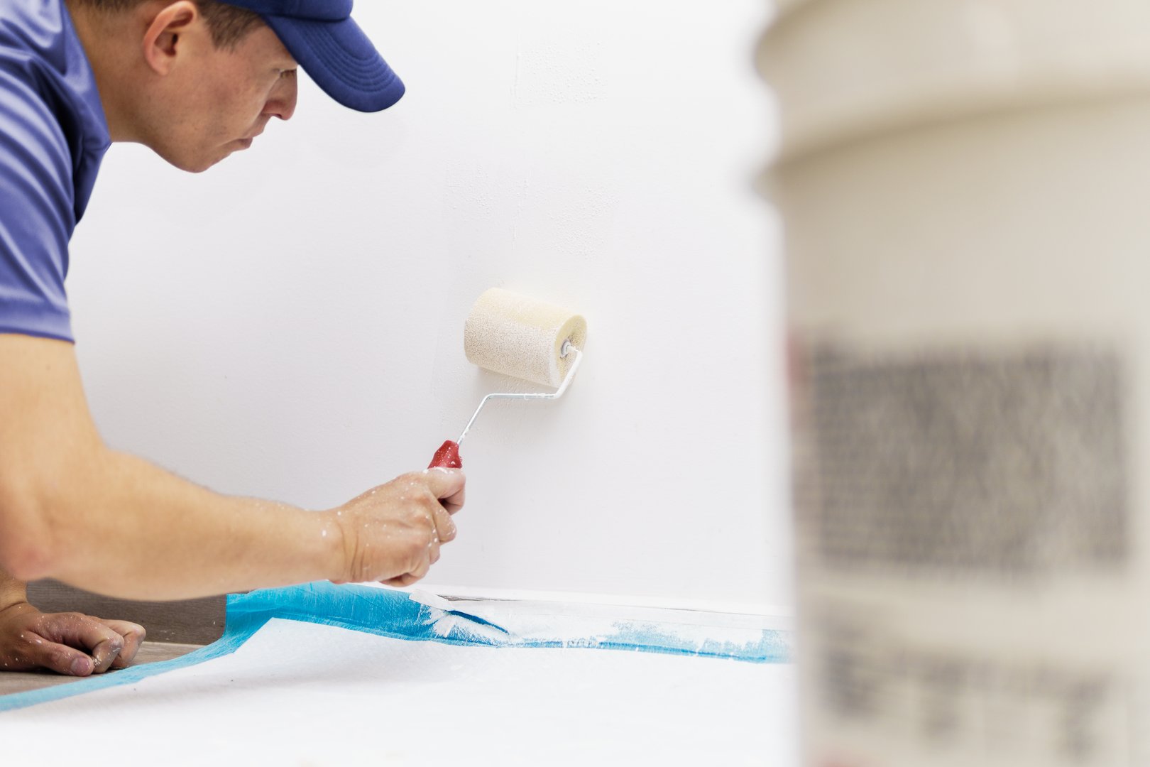 a young man painting the bottom of a house wall in color with a paint pot and a roller