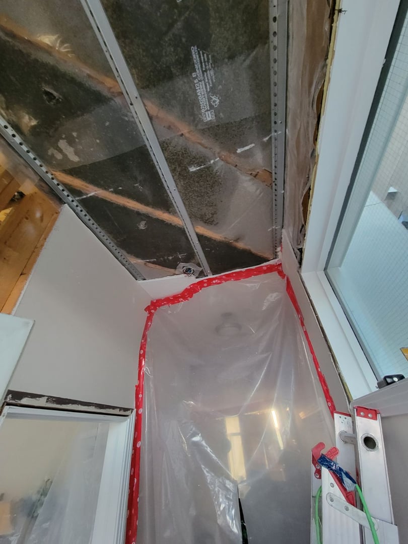 Ceiling renovation scene with exposed beams, plastic sheeting, and red tape framing the area.