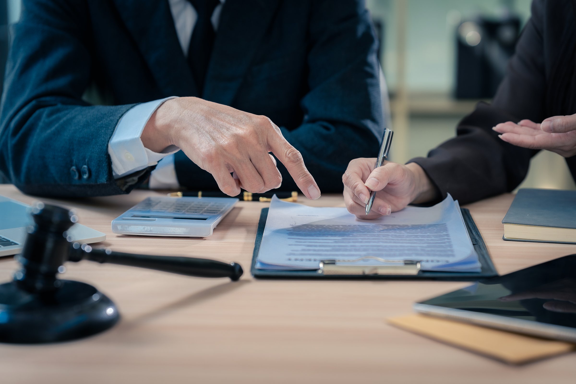 Law office with legal books and scales on table. Legal consultation: lawyer and client reviewing documents together. Representing trusts and legal proceedings. Close-up.
