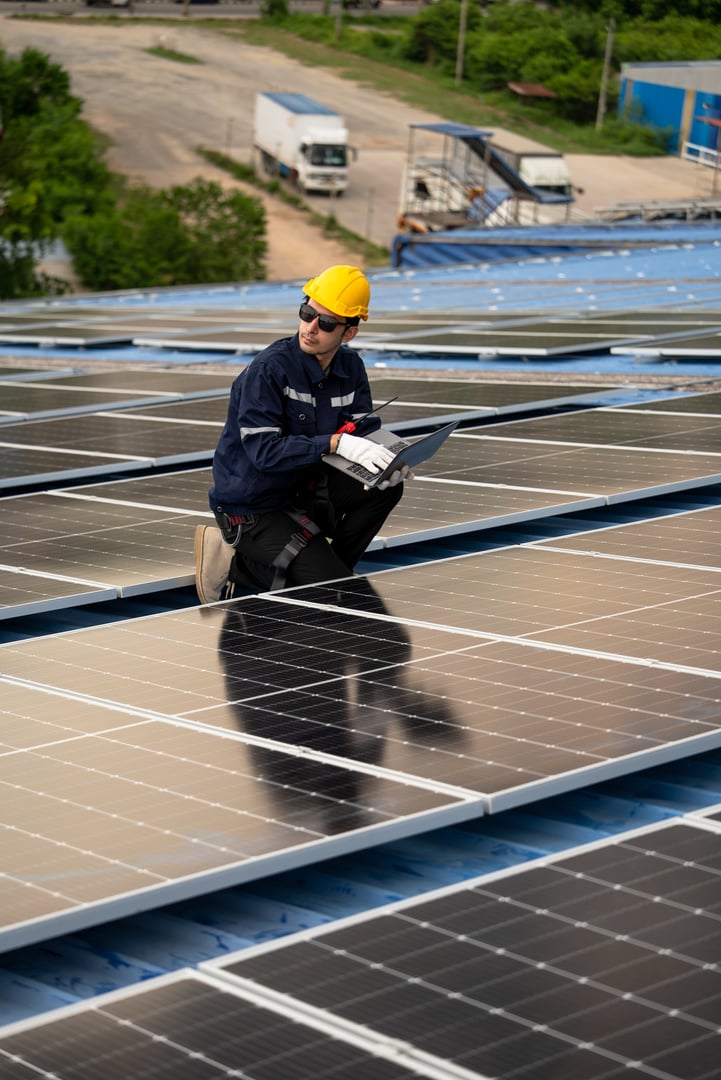 Male engineer checking solar cell or photovoltaic cell by computer laptop installed on the roof of the factory. Technician worker repair or inspect the system. Industrial renewable energy concept