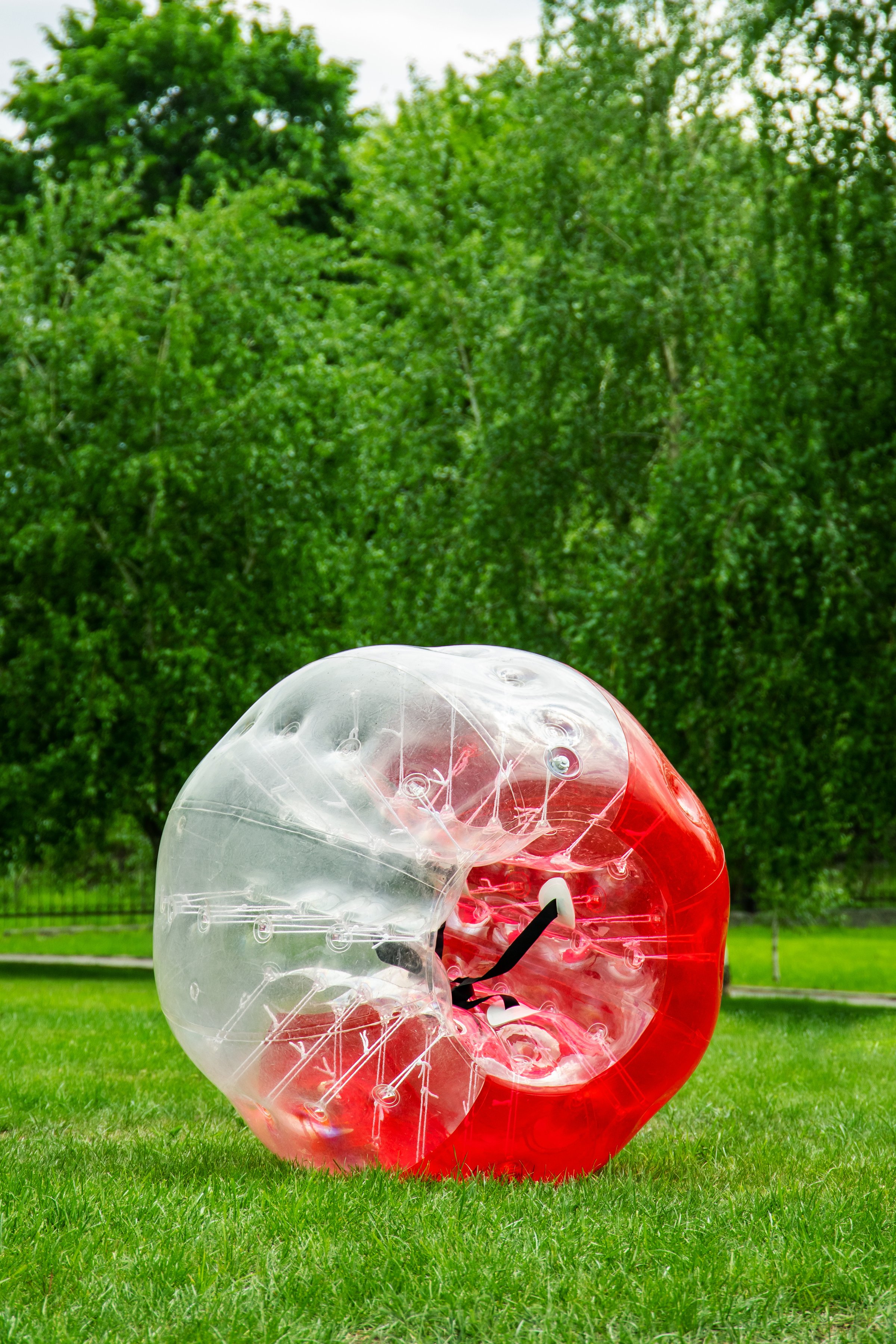 Red Zorbing Balloon on the summer lawn. Inflatable zorb ball outdoor. Leisure activity concept with vertical copy space.