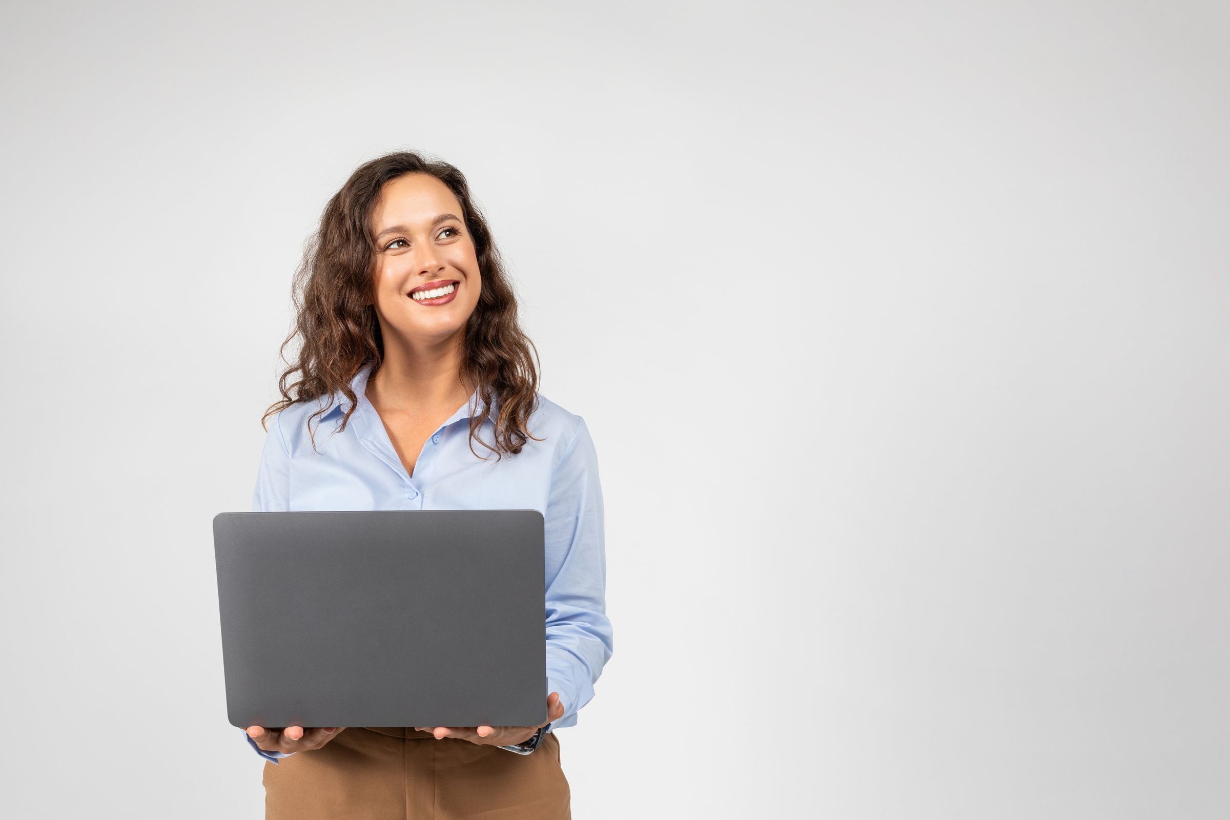 Positive caucasian millennial businesswoman typing on computer, chatting, look at empty space, isolated on gray studio background